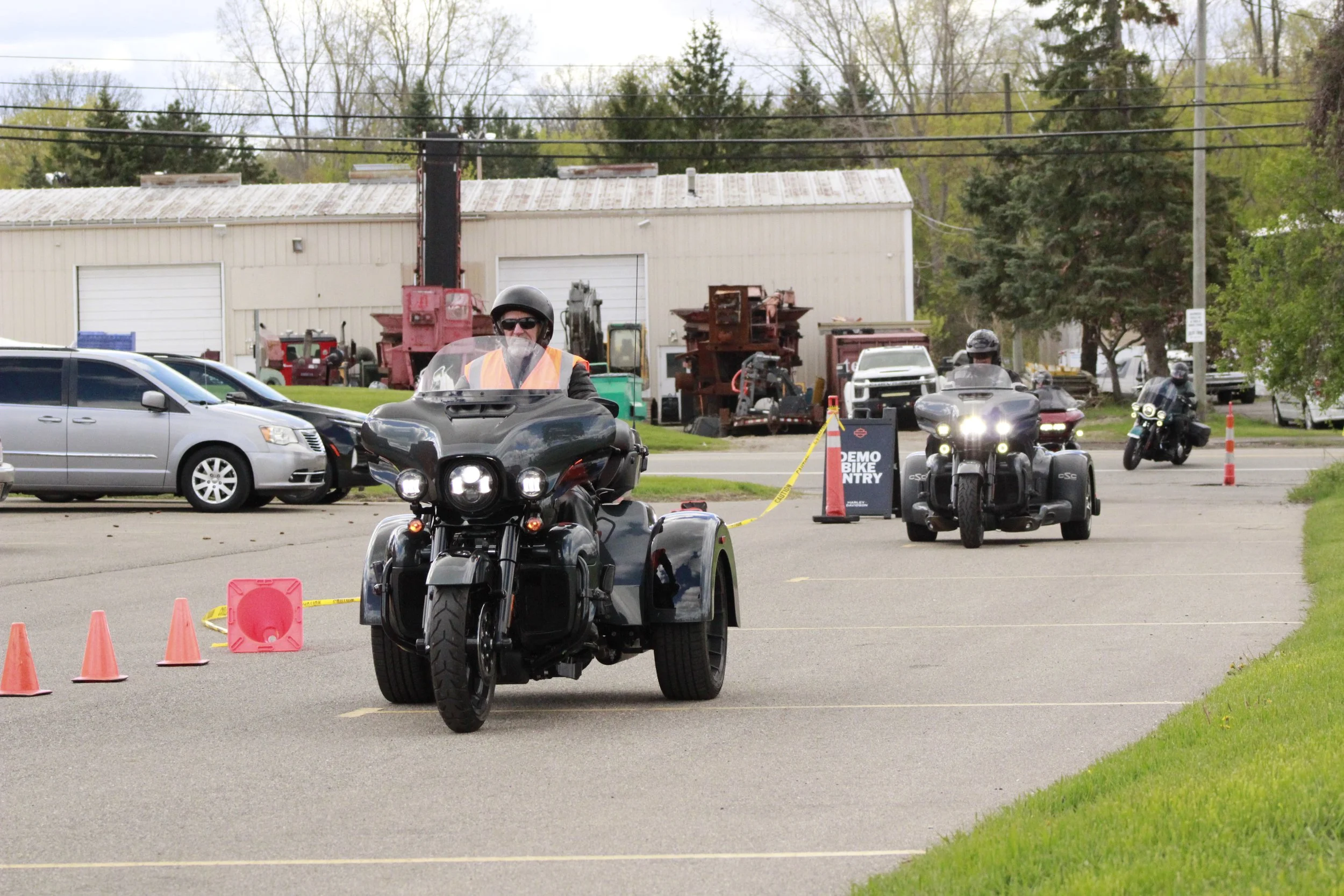 Motorcycles and cars at a police motorcycle training event with traffic cones and a sign that reads 'Demo Bike Entry' on a parking lot.