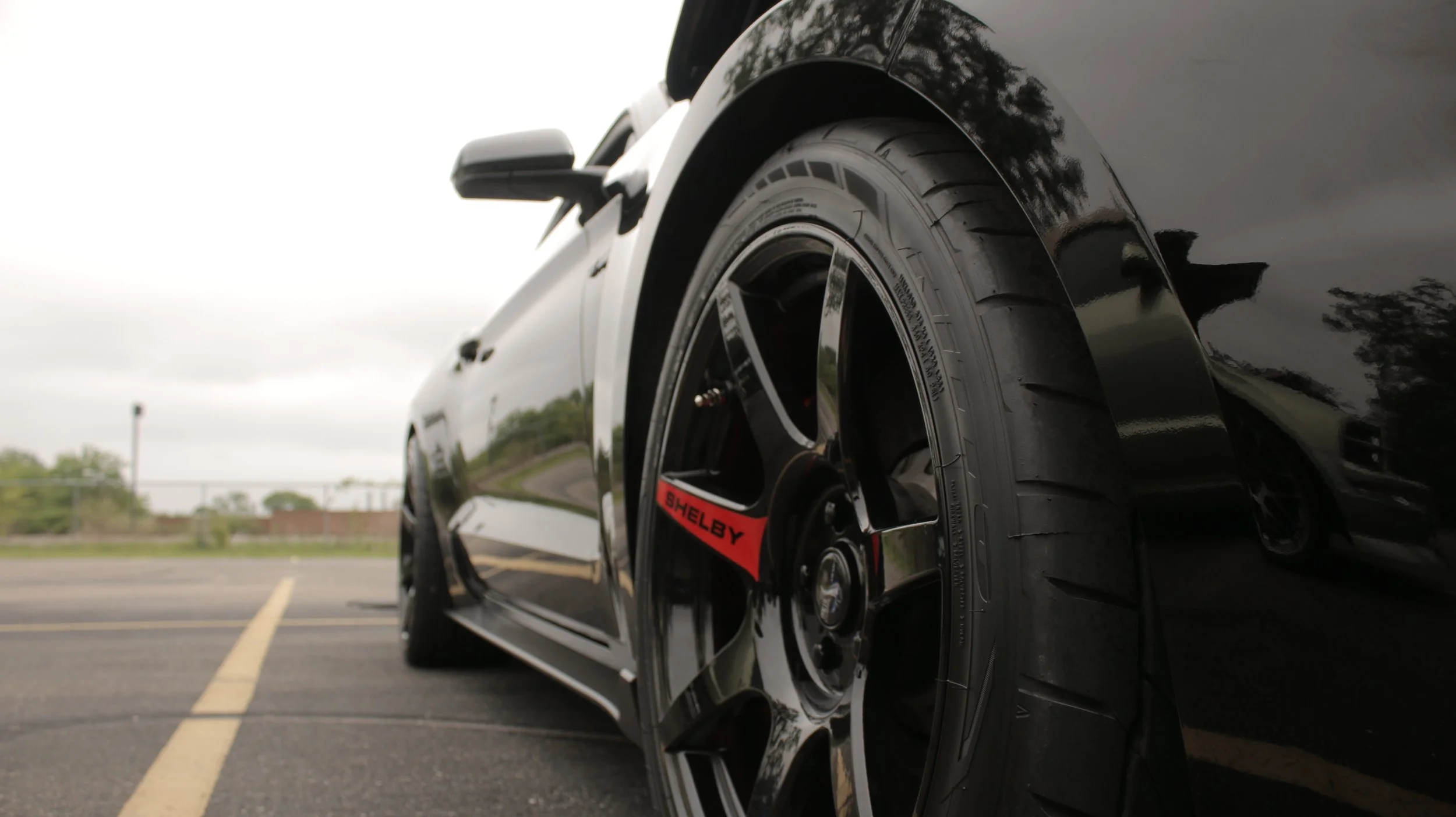 Close-up of a black racing car's wheel and tire parked in an empty parking lot.