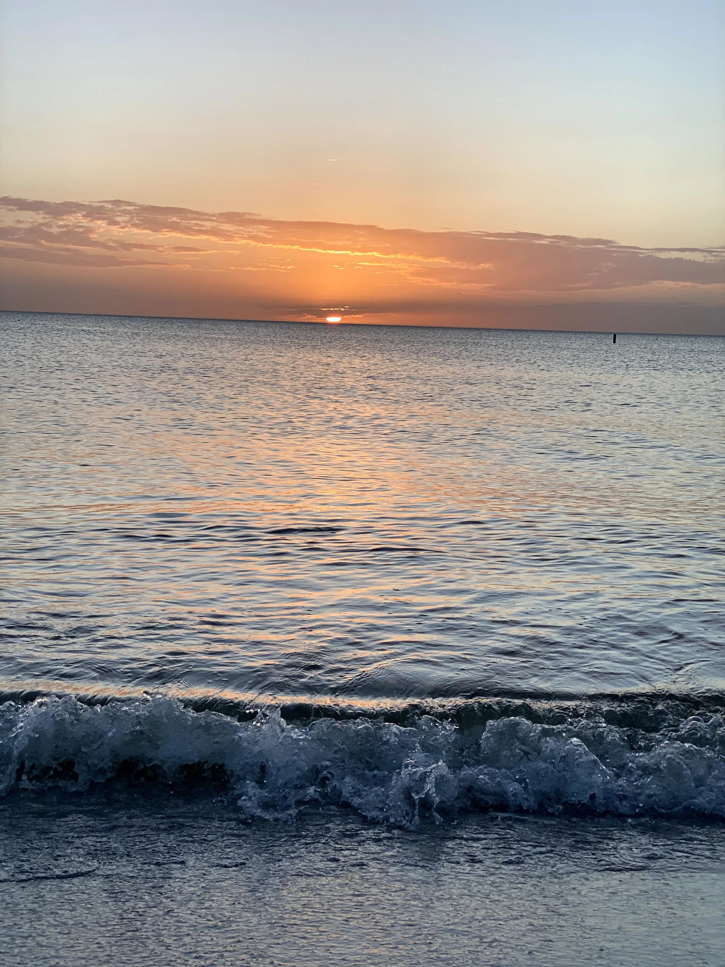 A scenic view of a sunset over the ocean with the sun partially below the horizon, colorful clouds, and gentle waves.