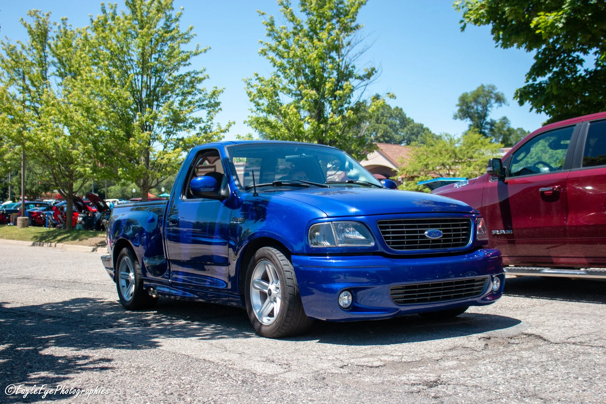 A blue pickup truck parked in a parking lot with trees and other vehicles in the background.