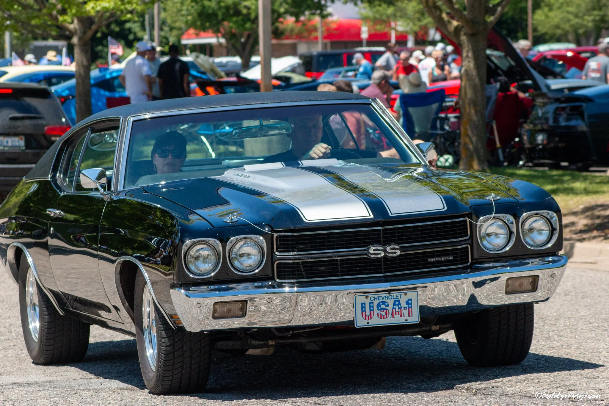 A black Chevrolet Chevelle SS with white racing stripes at a car show, with people gathered in the background.