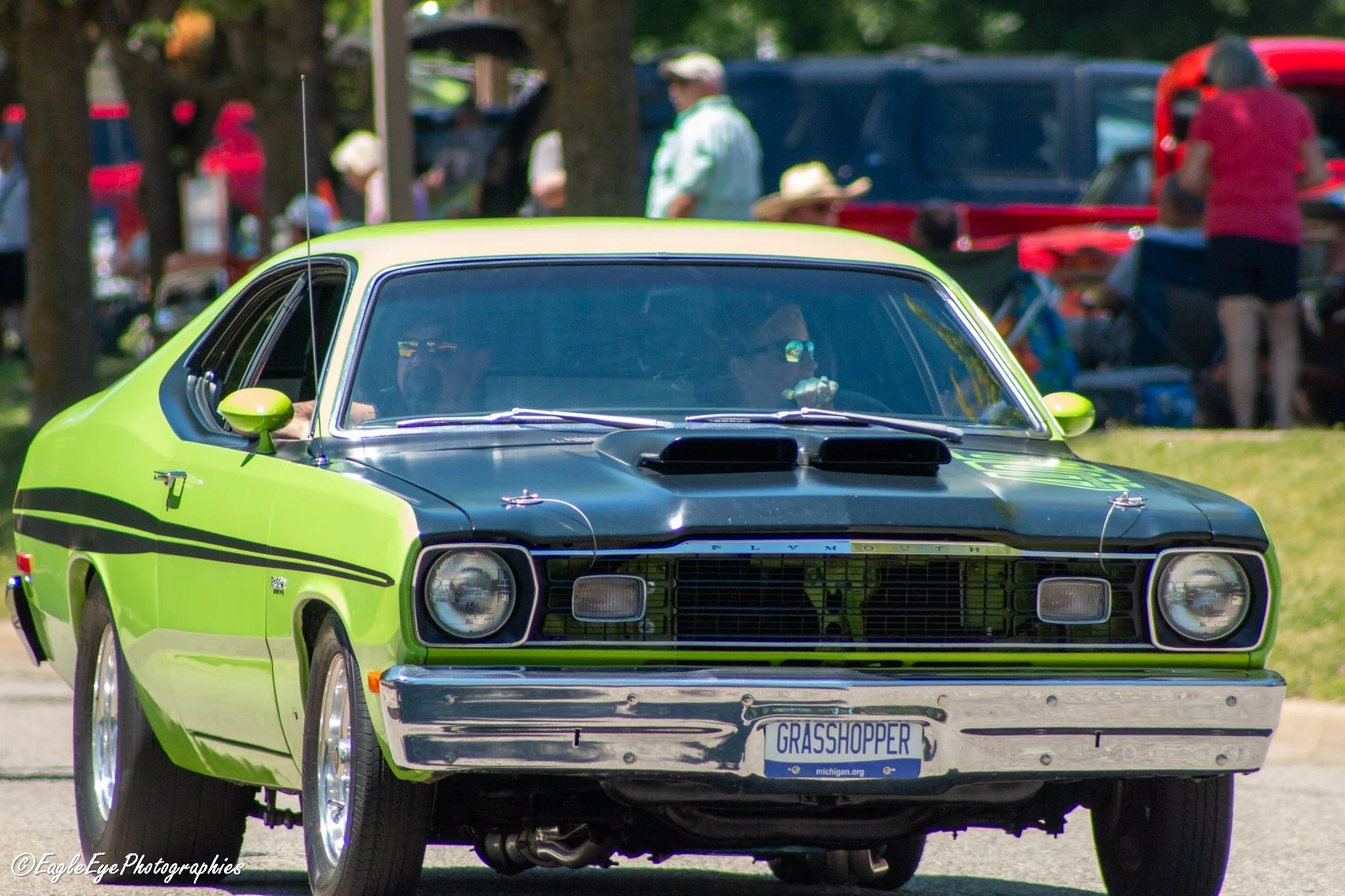 A lime green and black Plymouth car with a custom license plate that says 'GRASSHOPPER' parked outdoors at what appears to be a car show or gathering.