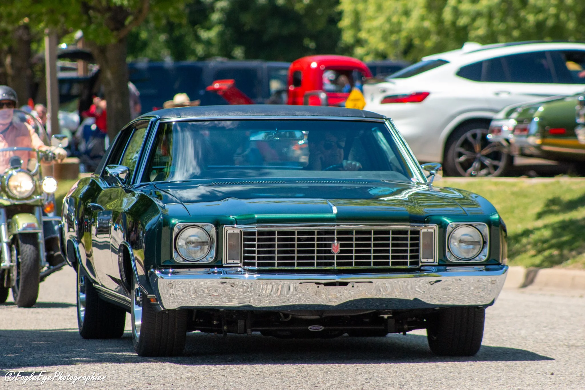 A black vintage car, possibly a Chevrolet, parked on a grassy area at a car show with other classic and modern cars and people in the background.
