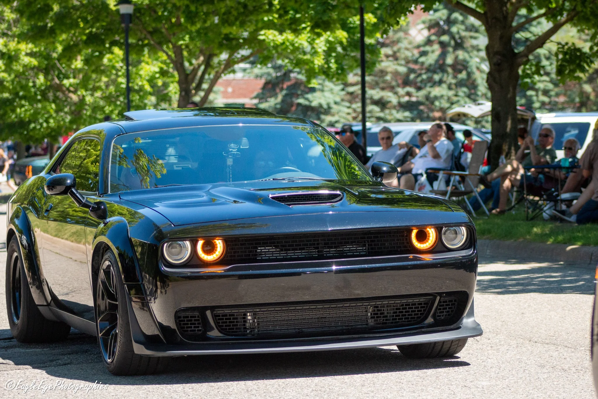 A black sports car driving on a street with green trees and spectators in the background
