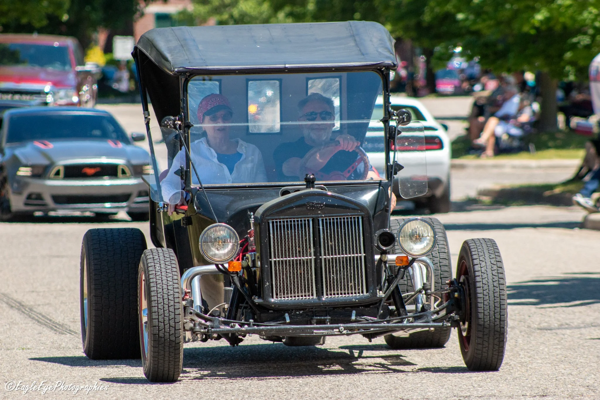 A golf cart with two passengers driving down a street.