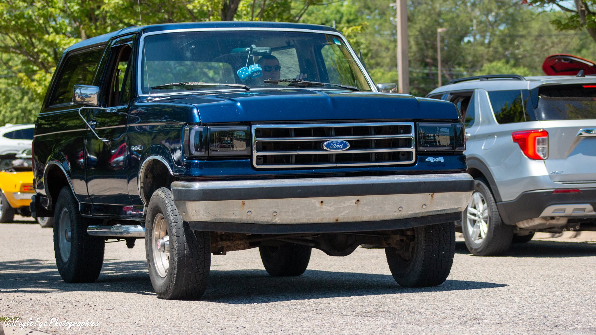 A blue Ford van parked among other vehicles in a parking lot surrounded by green trees.