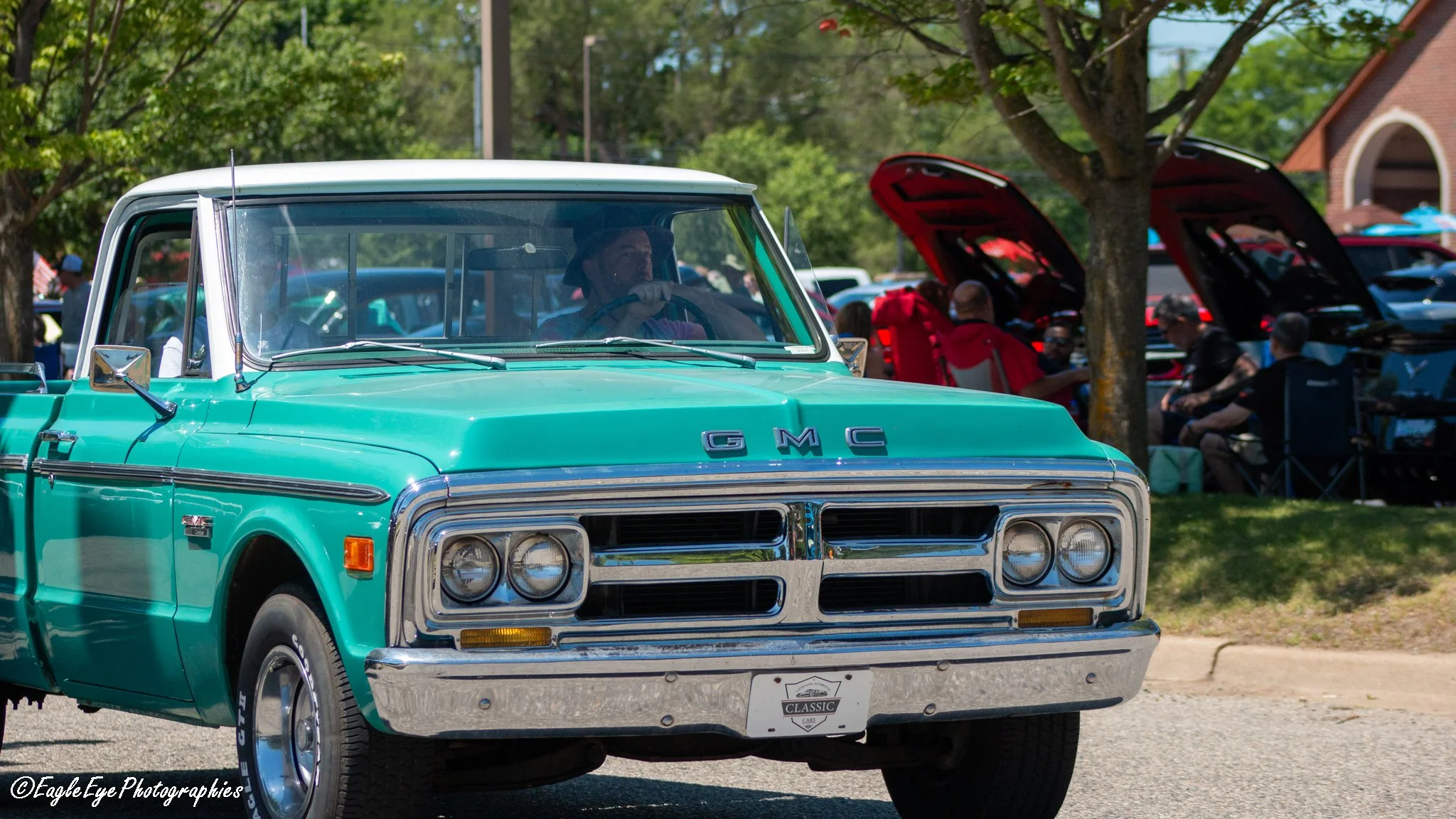 A vintage turquoise GMC pickup truck at a car show, with people and cars in the background.