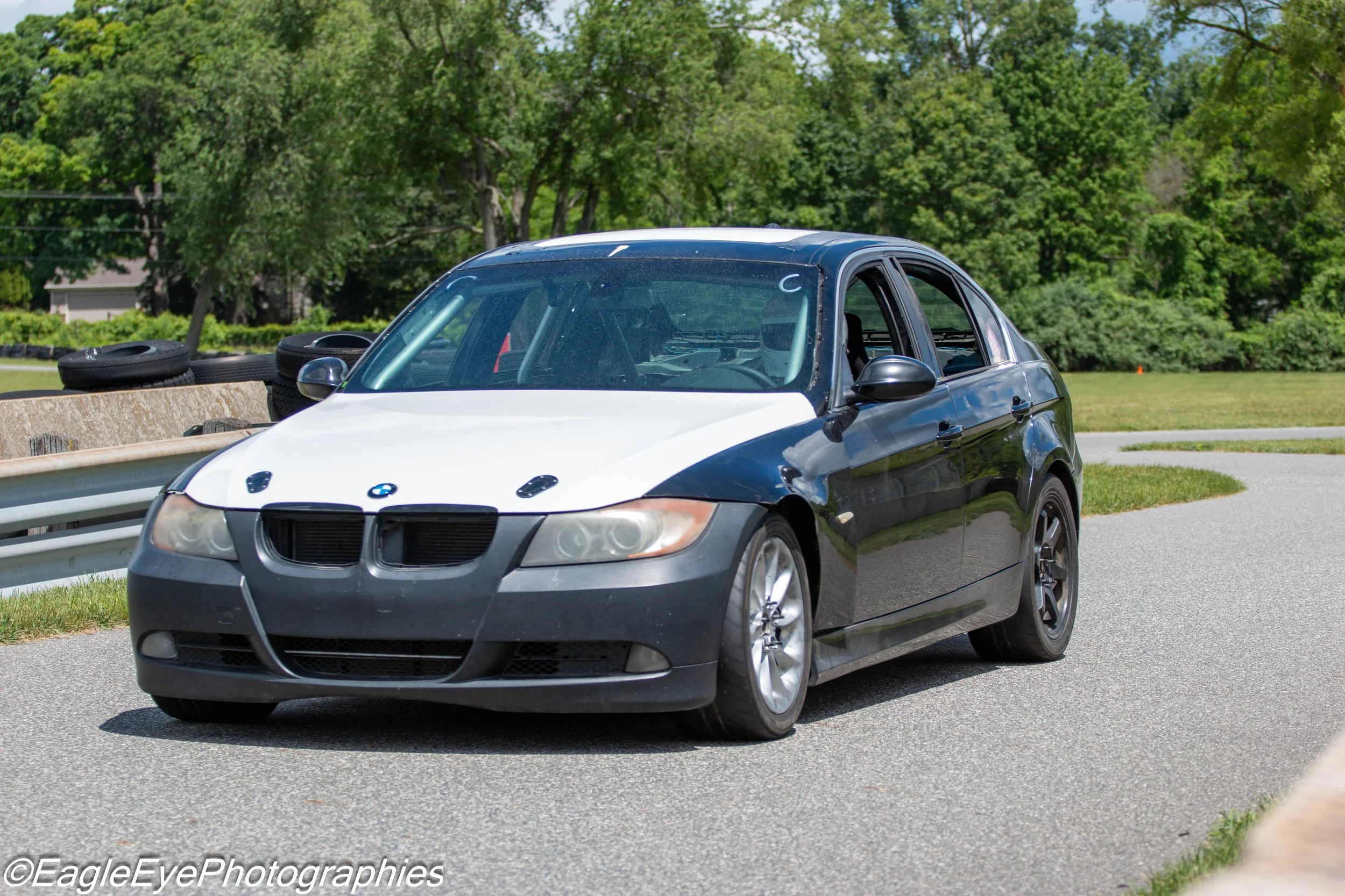 A black and white BMW sedan parked on the side of a road with a grassy area and trees in the background.