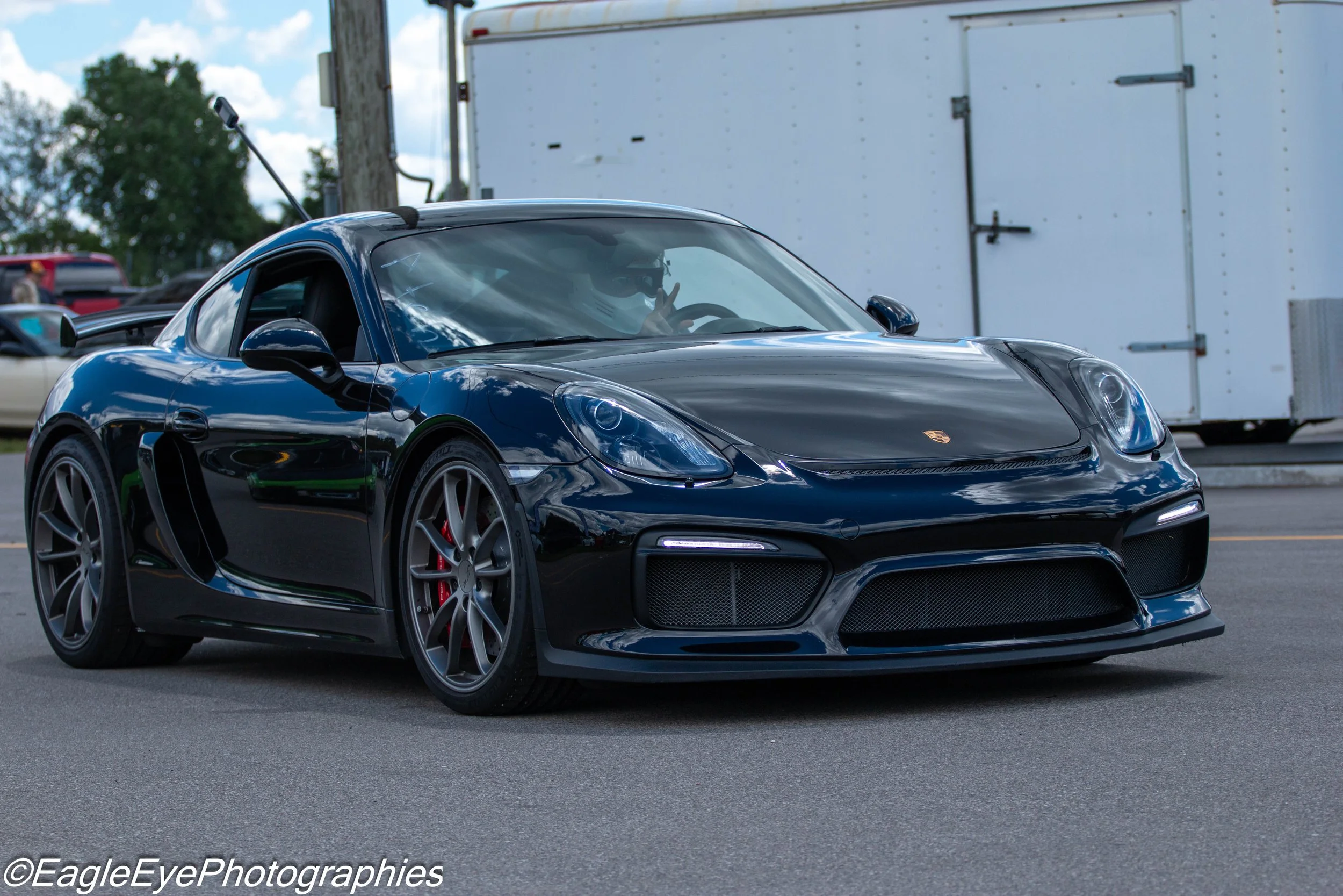 A black Porsche sports car with a driver making a peace sign gesture.