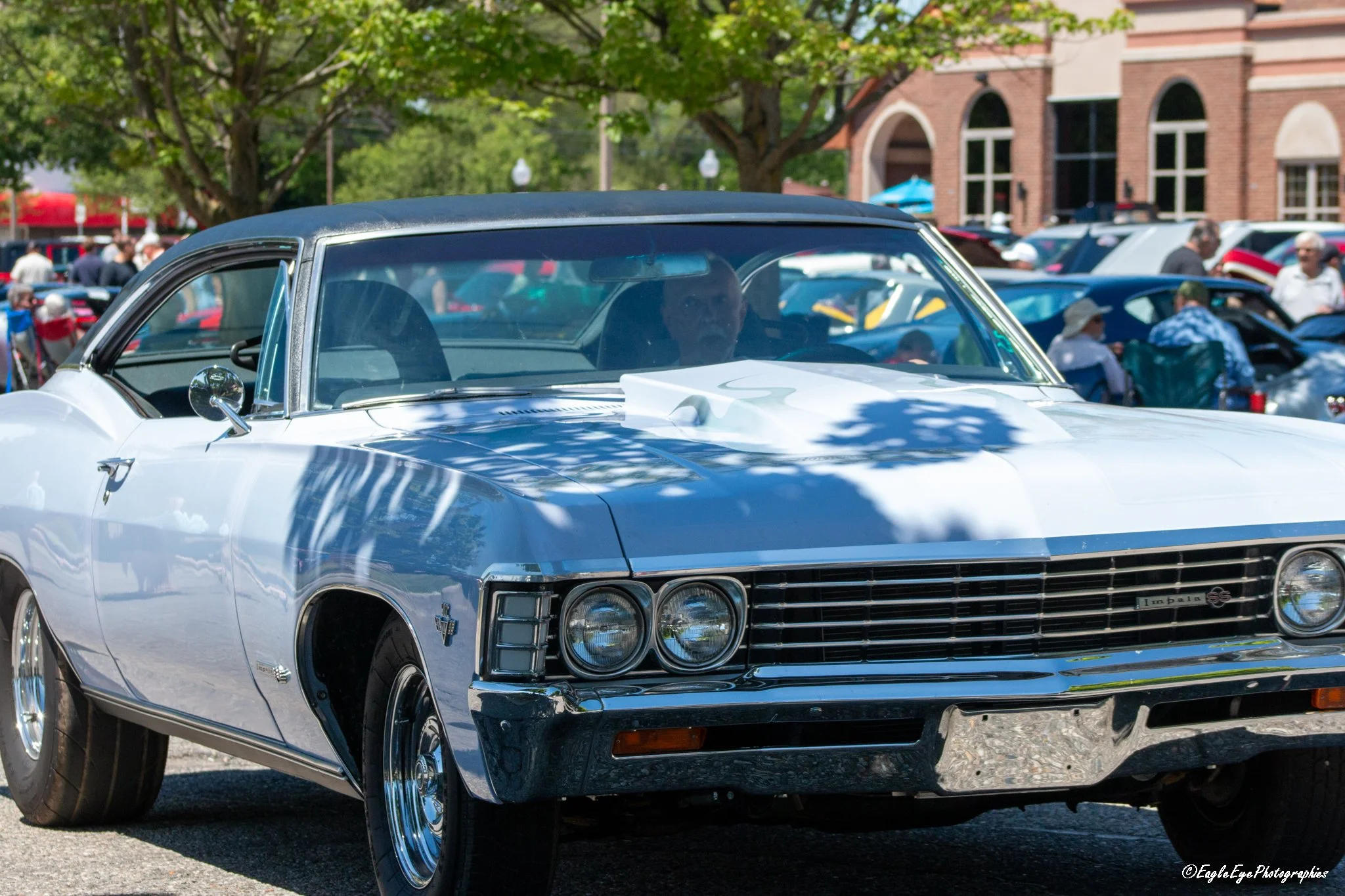 A white vintage Chevrolet Impala SS car parked at an outdoor car show with people in the background.