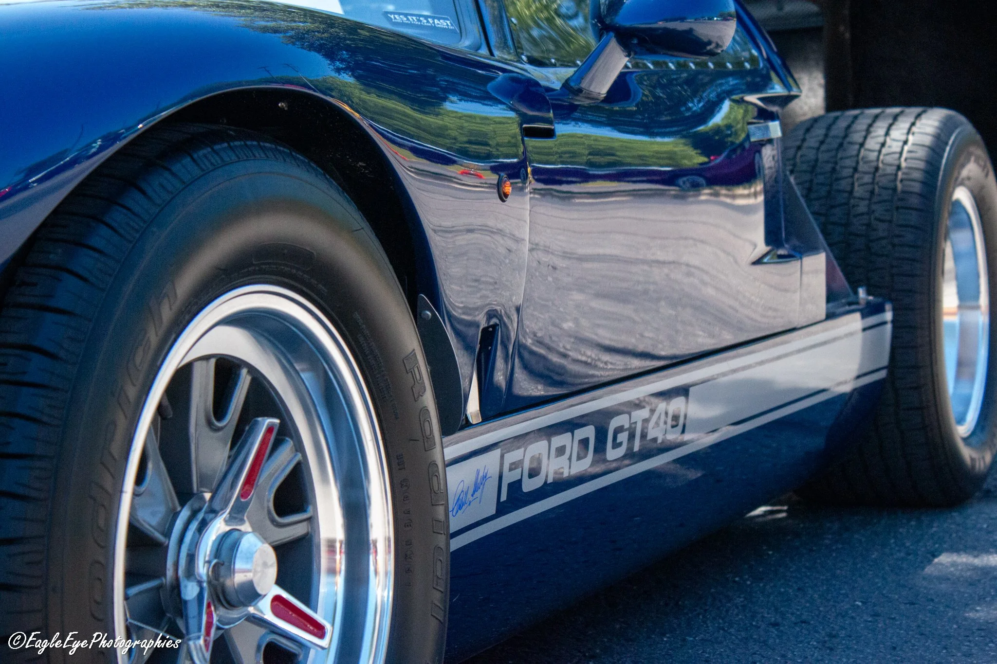 Close-up of a dark blue sports car showcasing its front wheel, side mirror, and part of the door with a sign that reads 'FORD GT40'.
