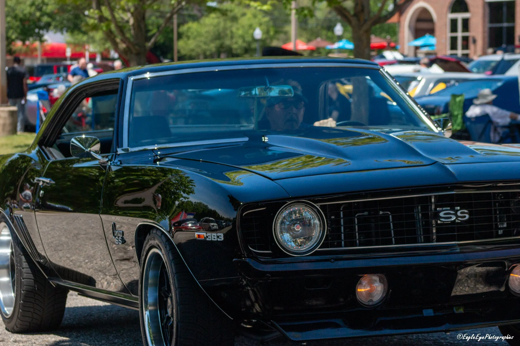 Black classic Chevrolet SS car parked at an outdoor event with people and tents in the background.