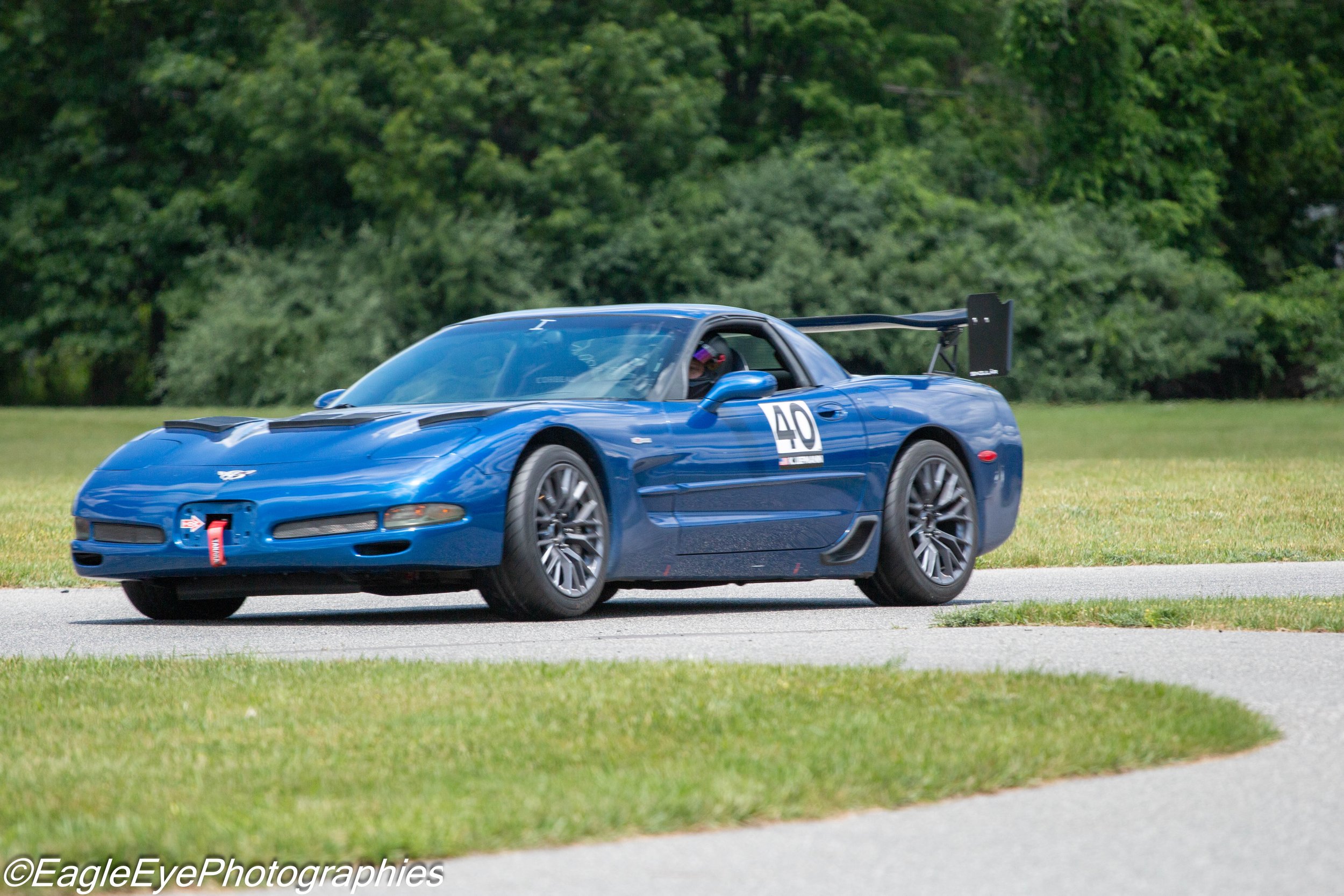 A blue sports car with race number 40 on the side, driving on a paved road surrounded by green grass and trees.