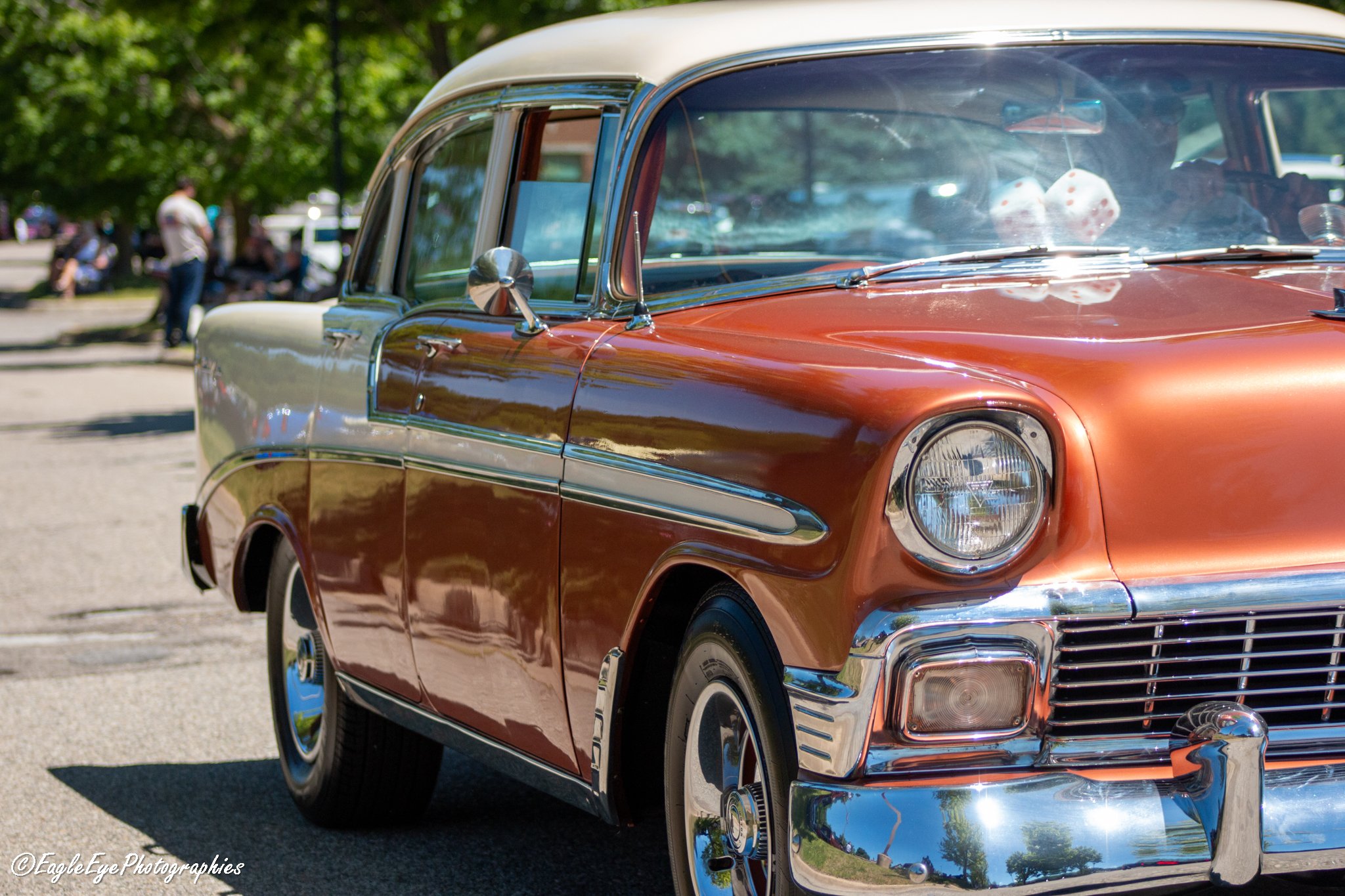 Vintage orange and silver classic car at an outdoor car show with people and trees in the background.