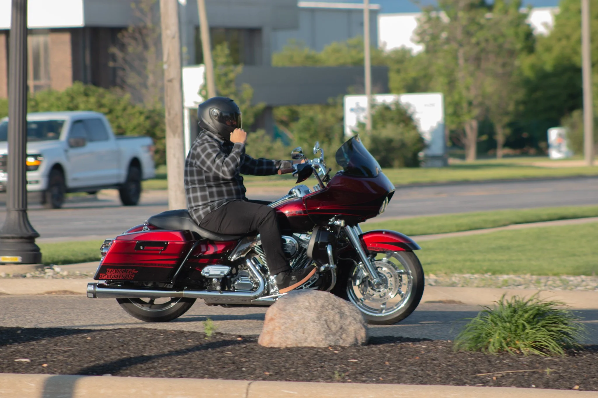 Person riding a red Harley-Davidson motorcycle on a city street, wearing a black helmet and checkered shirt.