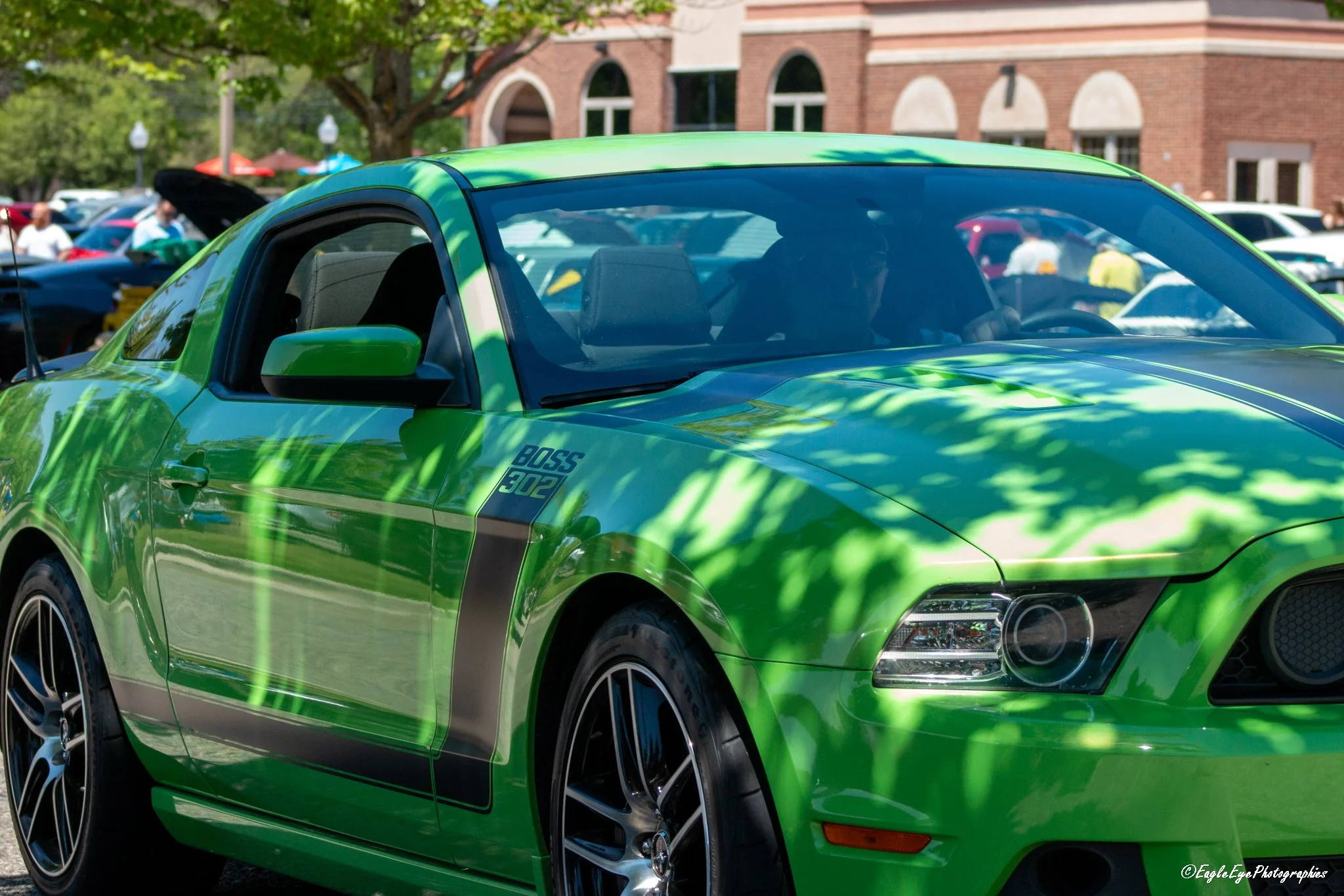A bright green sporty car parked outdoors during a car show in front of a brick building, with a crowd of people and other cars in the background.