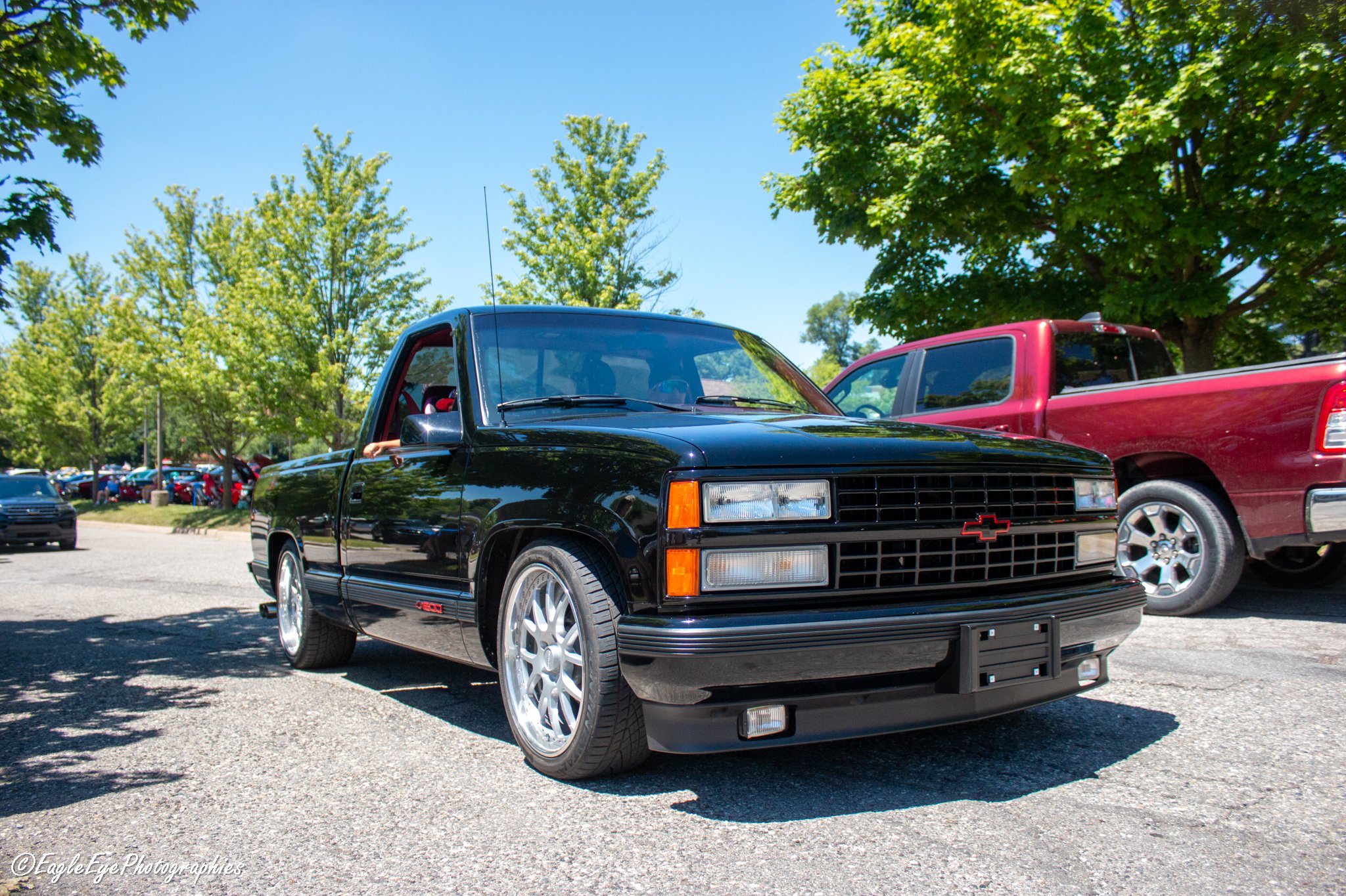 Black Chevrolet pickup truck parked in a parking lot surrounded by green trees on a sunny day.