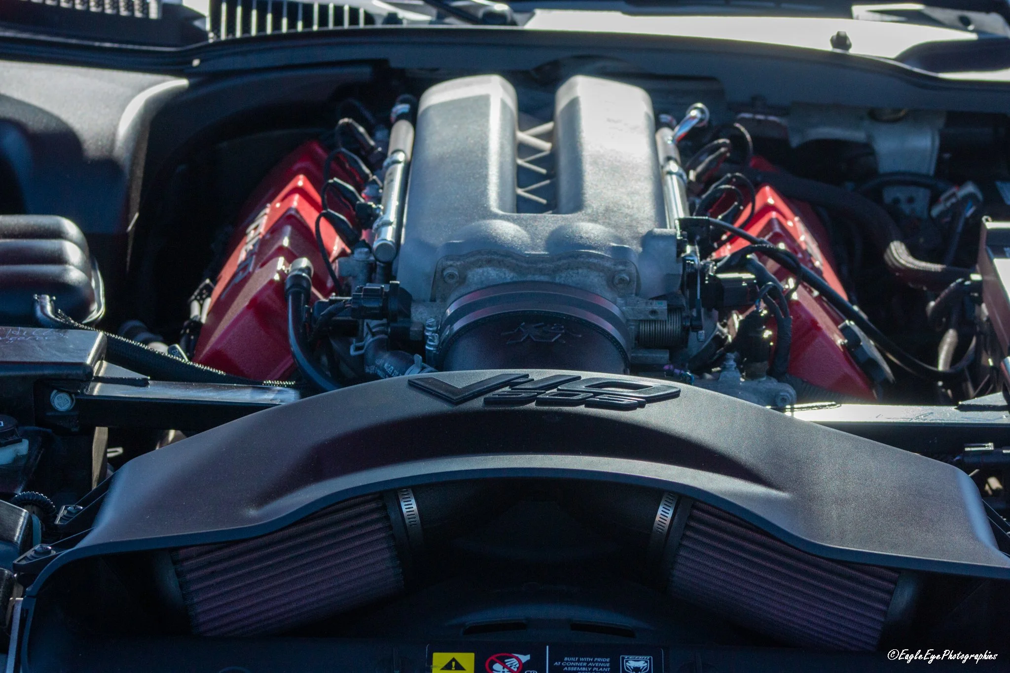 The image shows a close-up view of a car engine inside the engine bay of a vehicle, with a view from the front.
