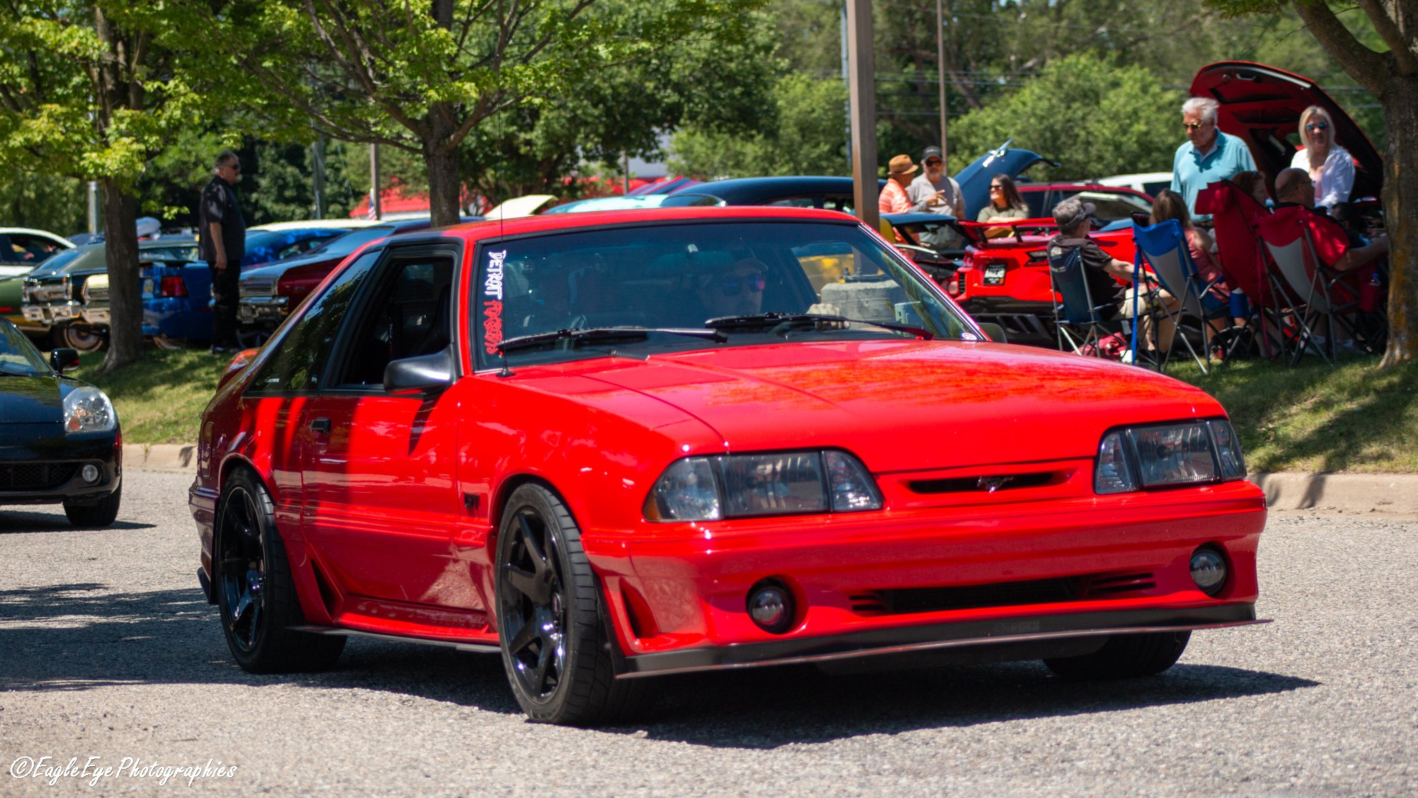 Red sports car parked at a car show with people and other cars in the background.