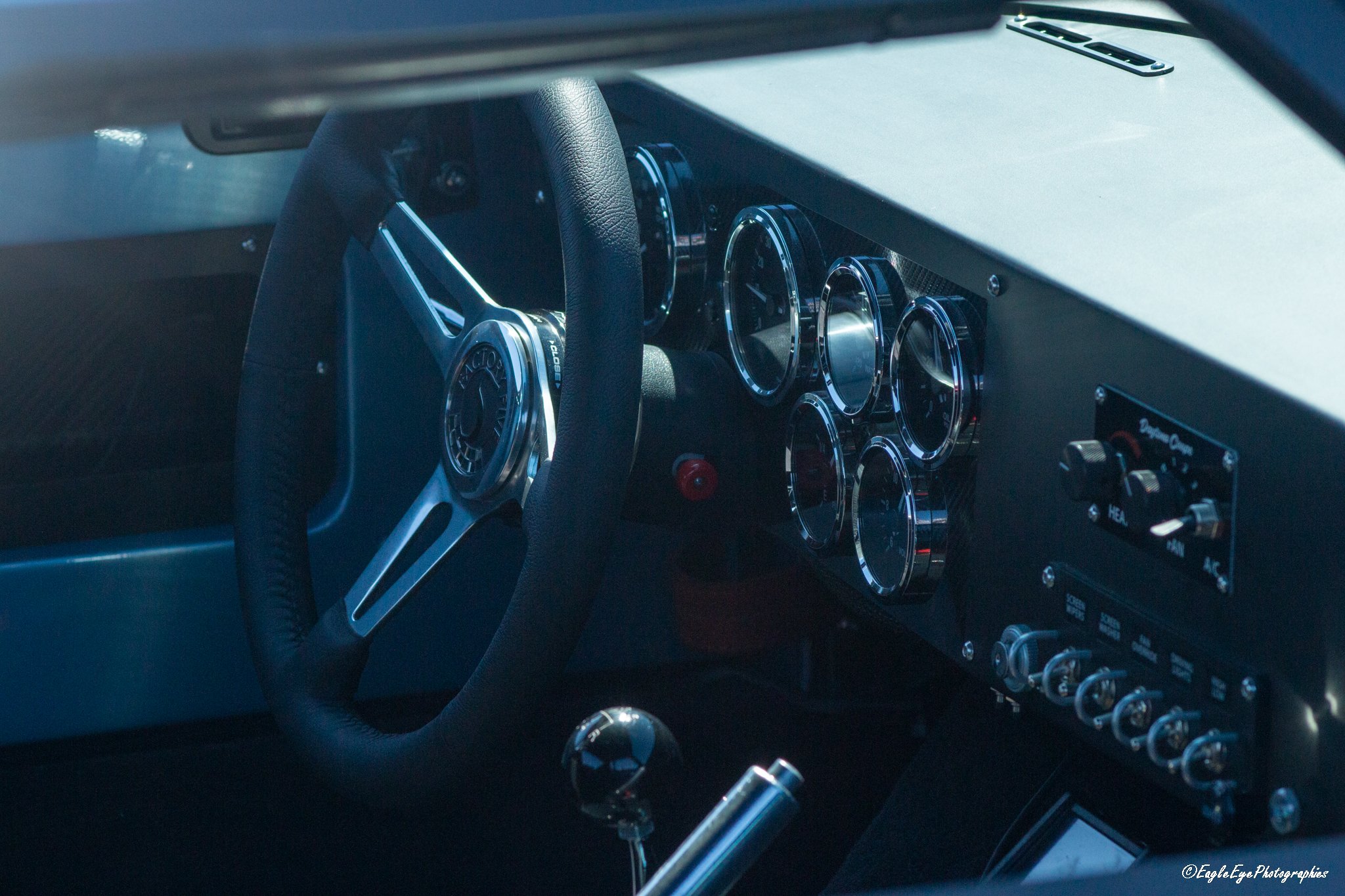 Close-up view of a car's dashboard and steering wheel, featuring multiple analog gauges and switches.