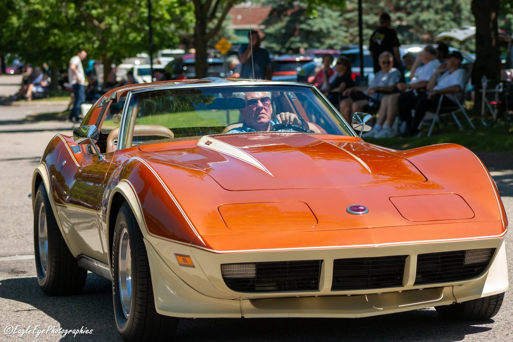 Orange classic Chevrolet Corvette at car show with people sitting and walking in background.