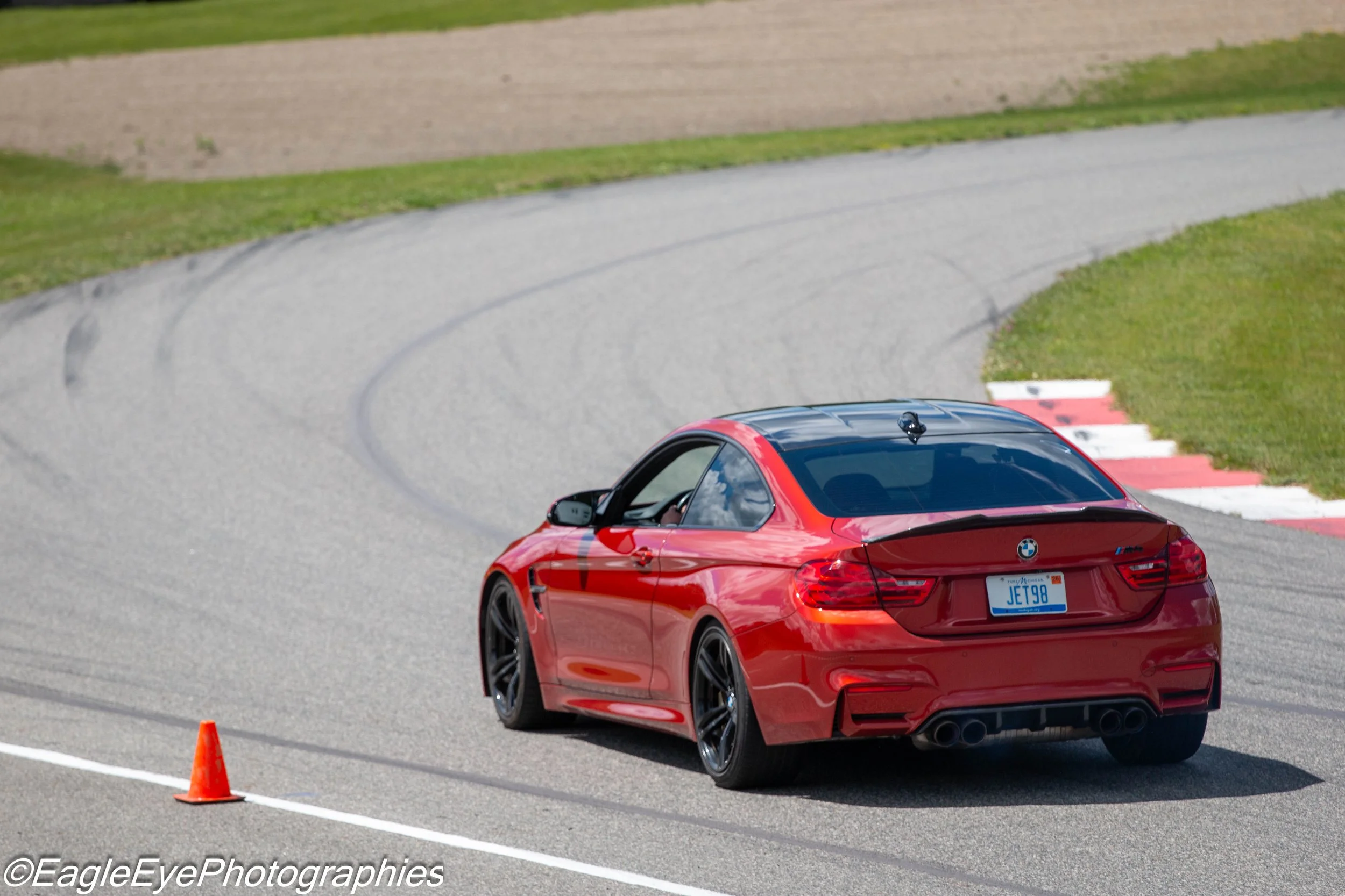 A red BMW sports car on a race track, with two orange traffic cones in front, appears to be in a driving or racing event.