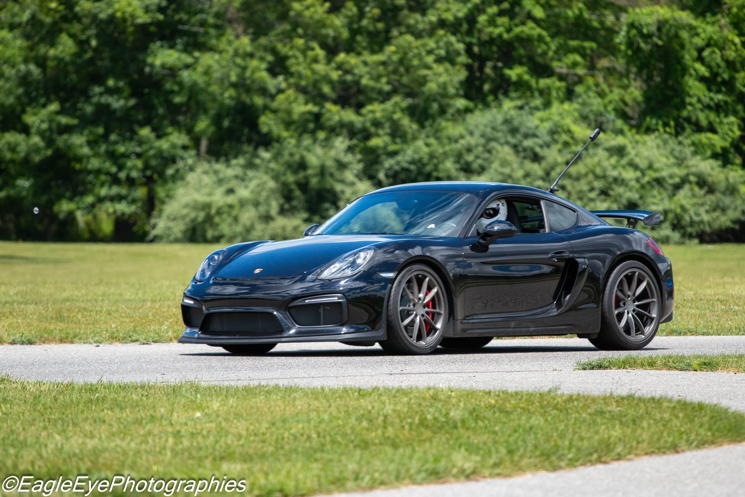 A black sports car driving on a road with green trees in the background.