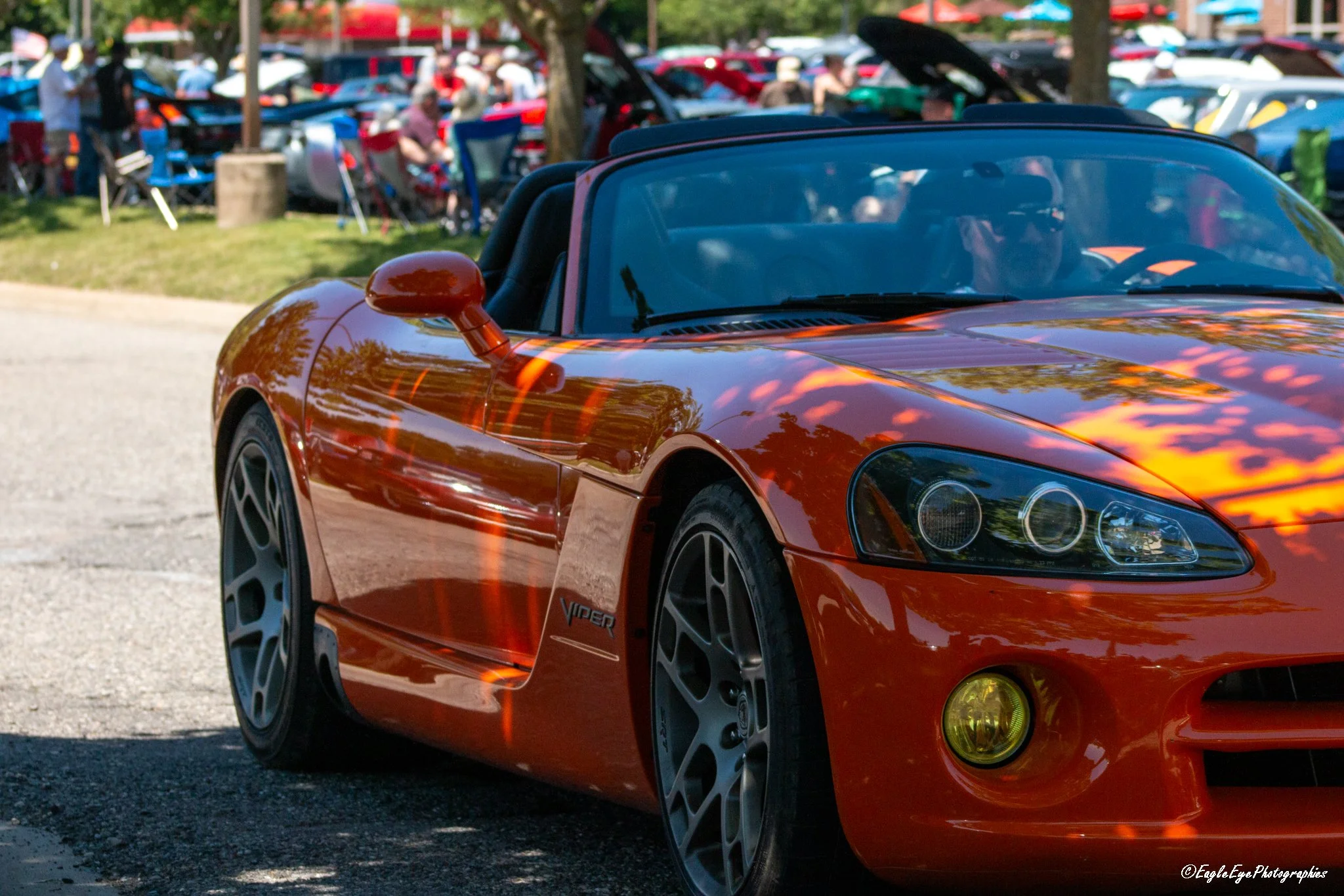 A red Chevrolet Corvette sports car parked outdoors at a car show, with people and other cars in the background.