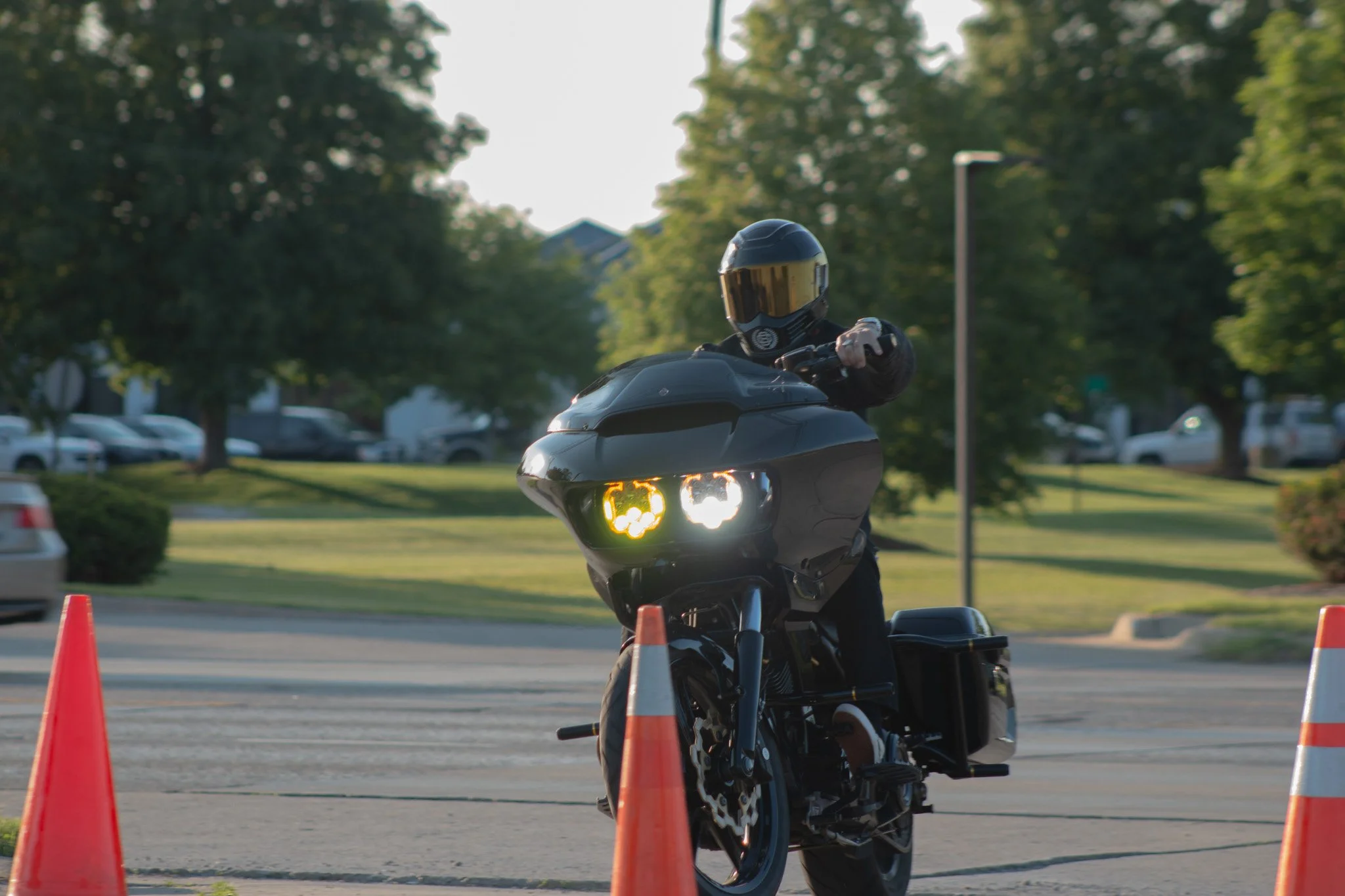 A person wearing a helmet riding a motorcycle between orange traffic cones during daytime in an outdoor parking lot.