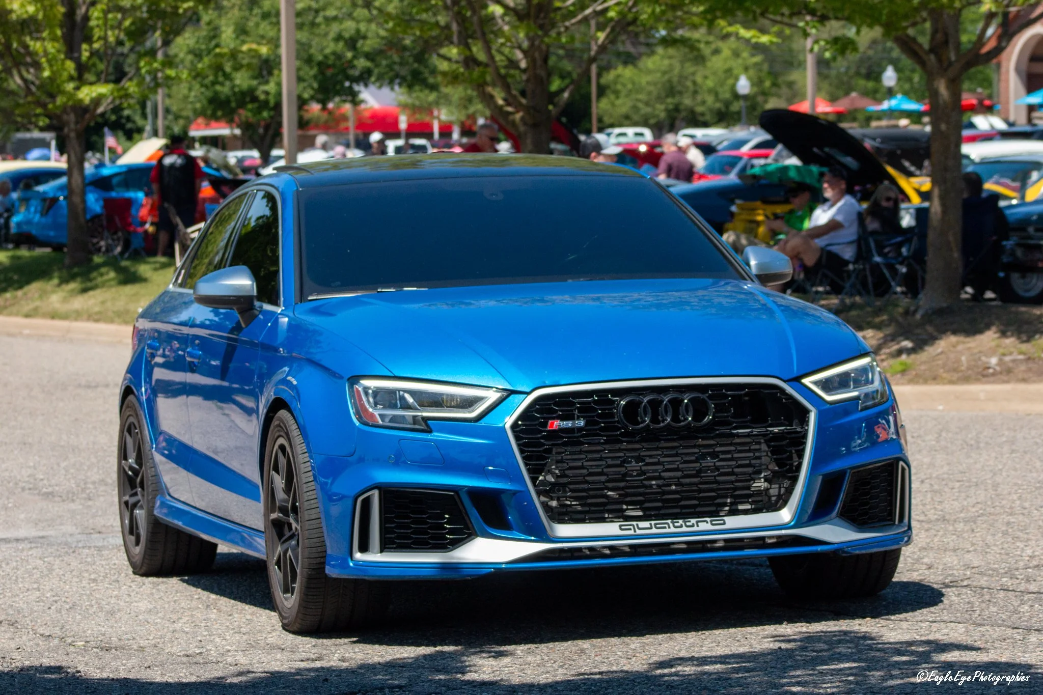 A blue Audi RS Q3 parked at a car show with several people and other cars in the background.