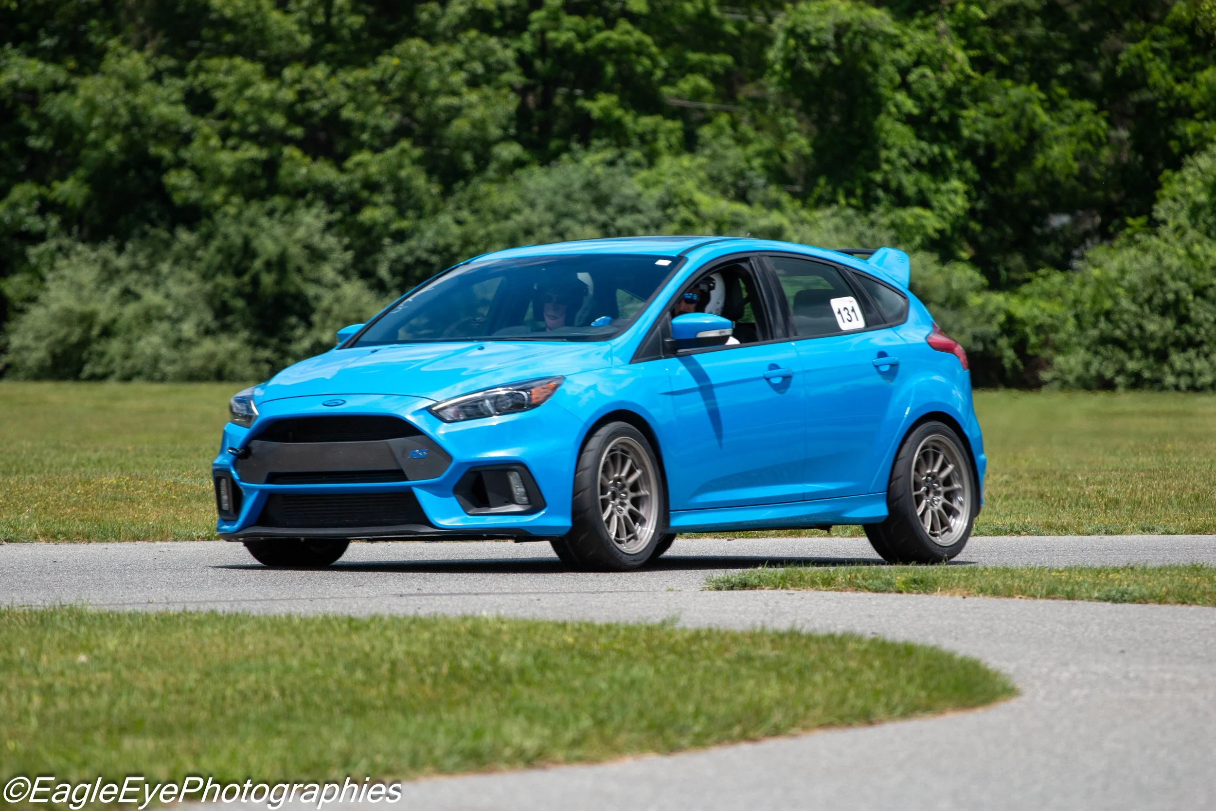 A blue hatchback car driving on a grassy field with trees in the background.