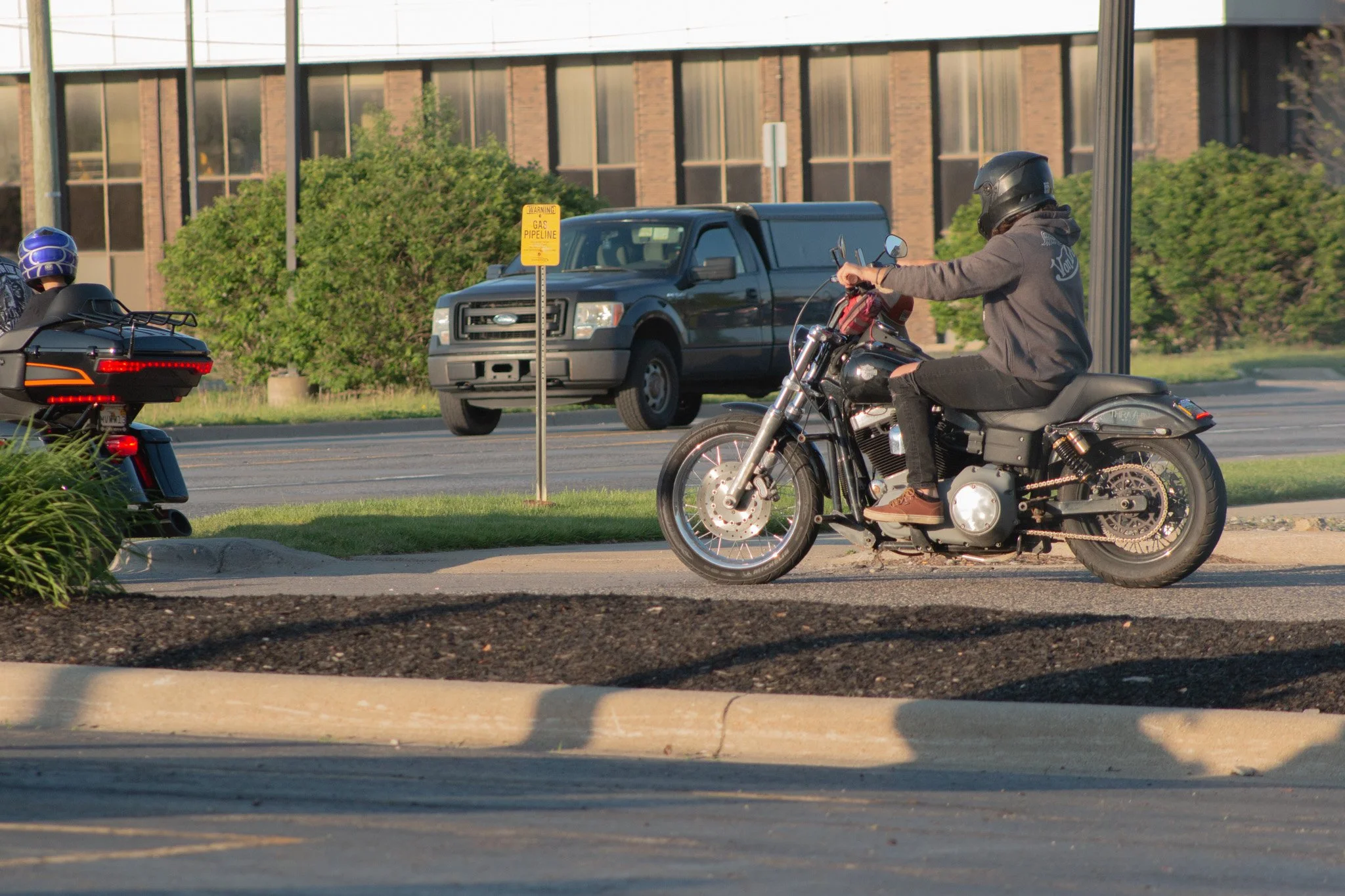 A person riding a black motorcycle with a helmet and casual clothing on a road.