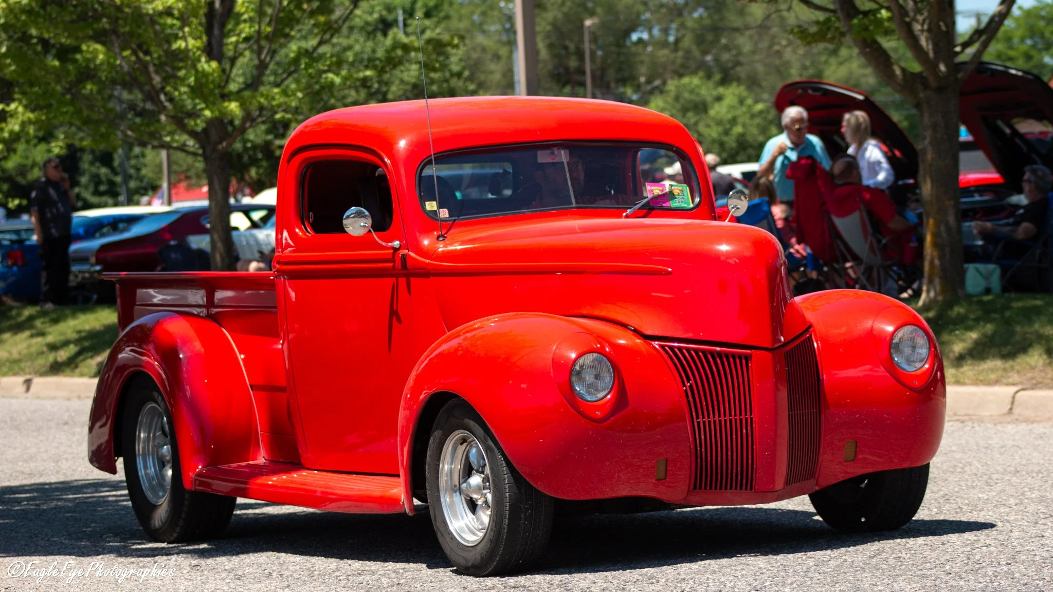 A vintage red pickup truck at a car show with people in the background.