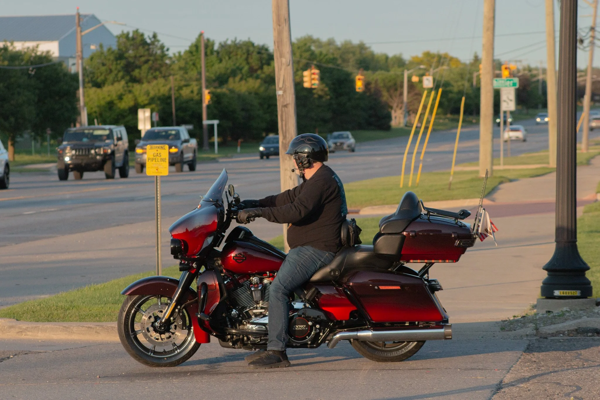 A man wearing a black helmet and black shirt riding a red motorcycle on a city sidewalk.
