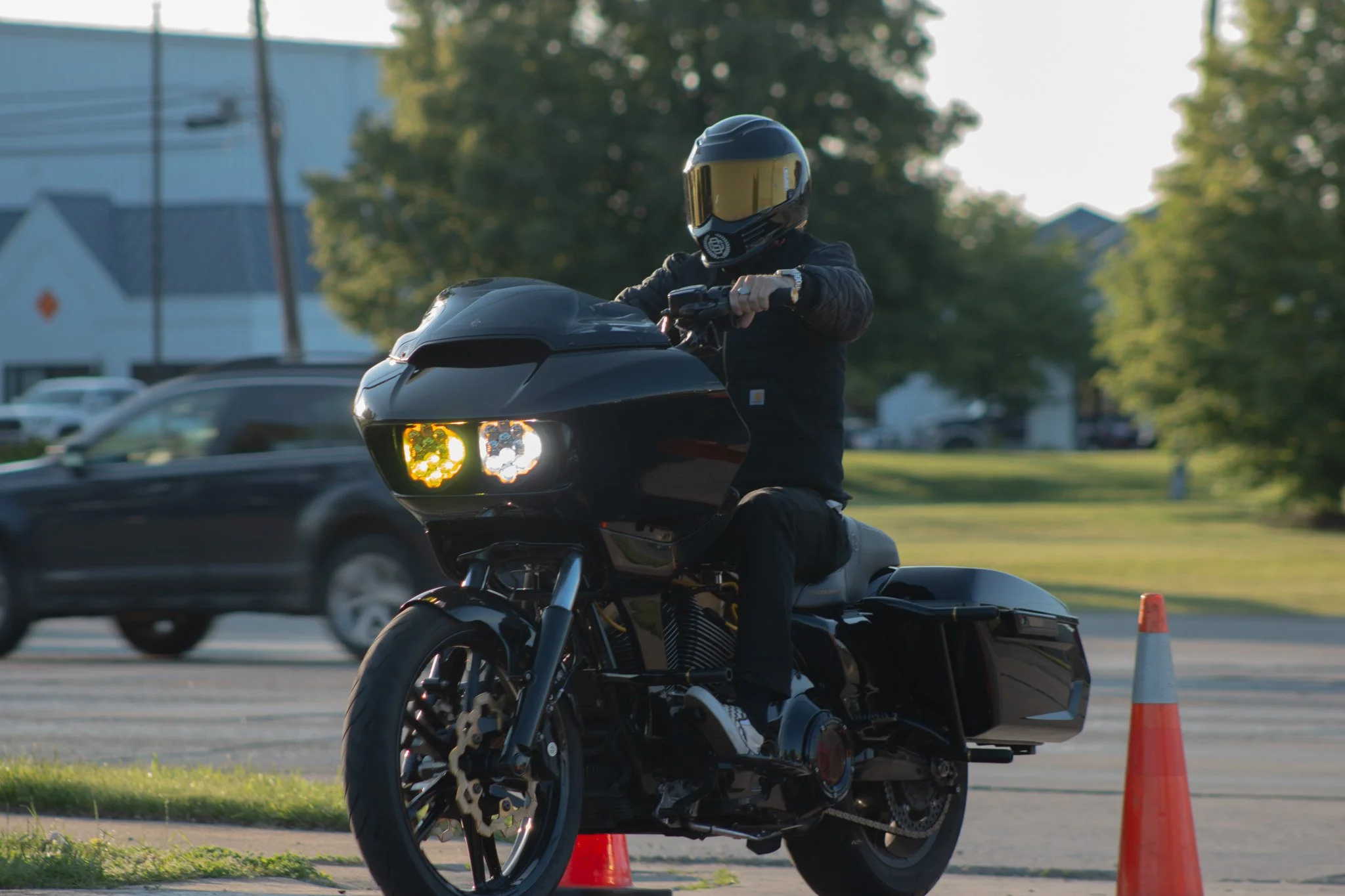 A person wearing a black motorcycle helmet and jacket riding a black motorcycle past orange traffic cones during daytime.