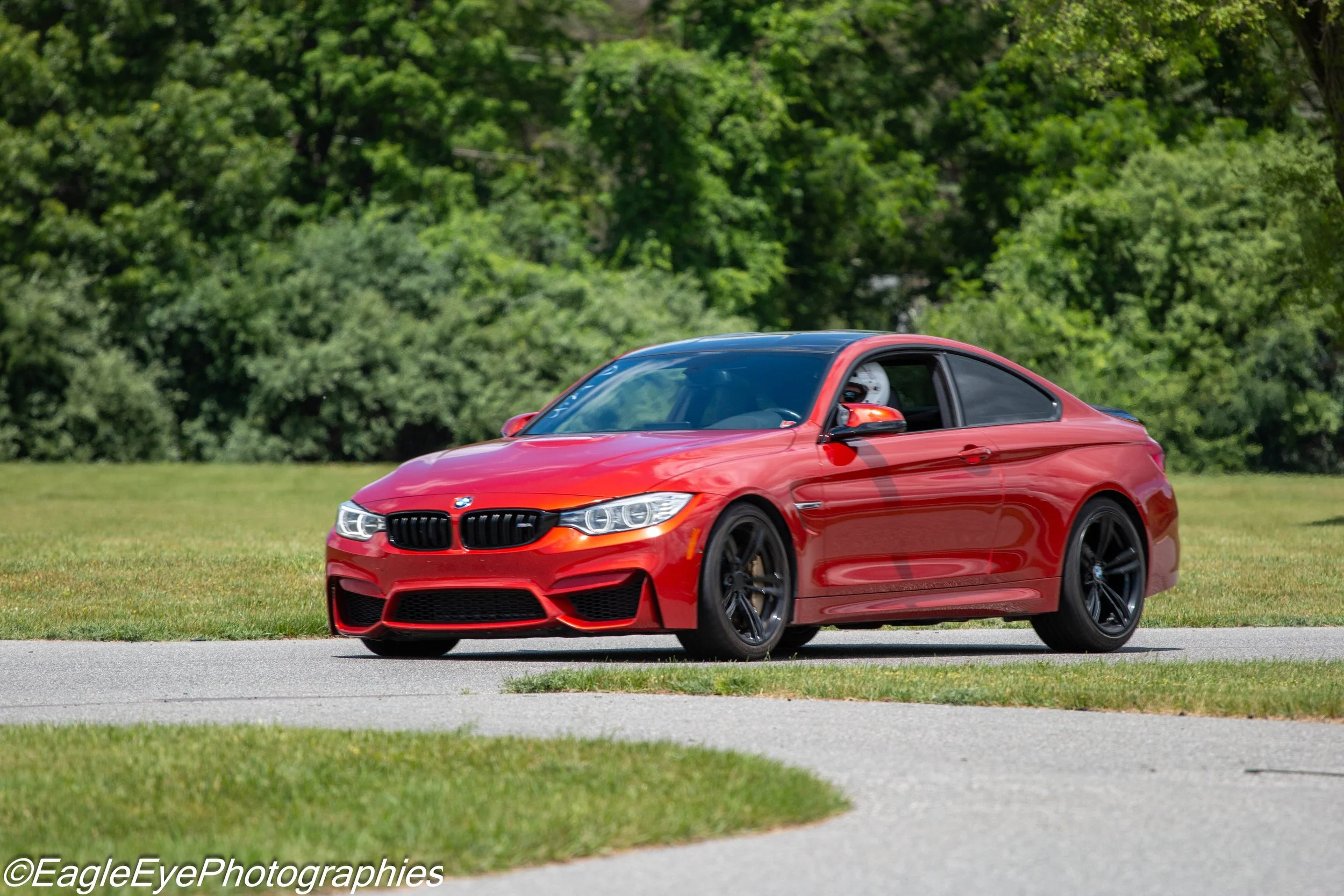 A red BMW coupe driving on a road with green trees and grass in the background.