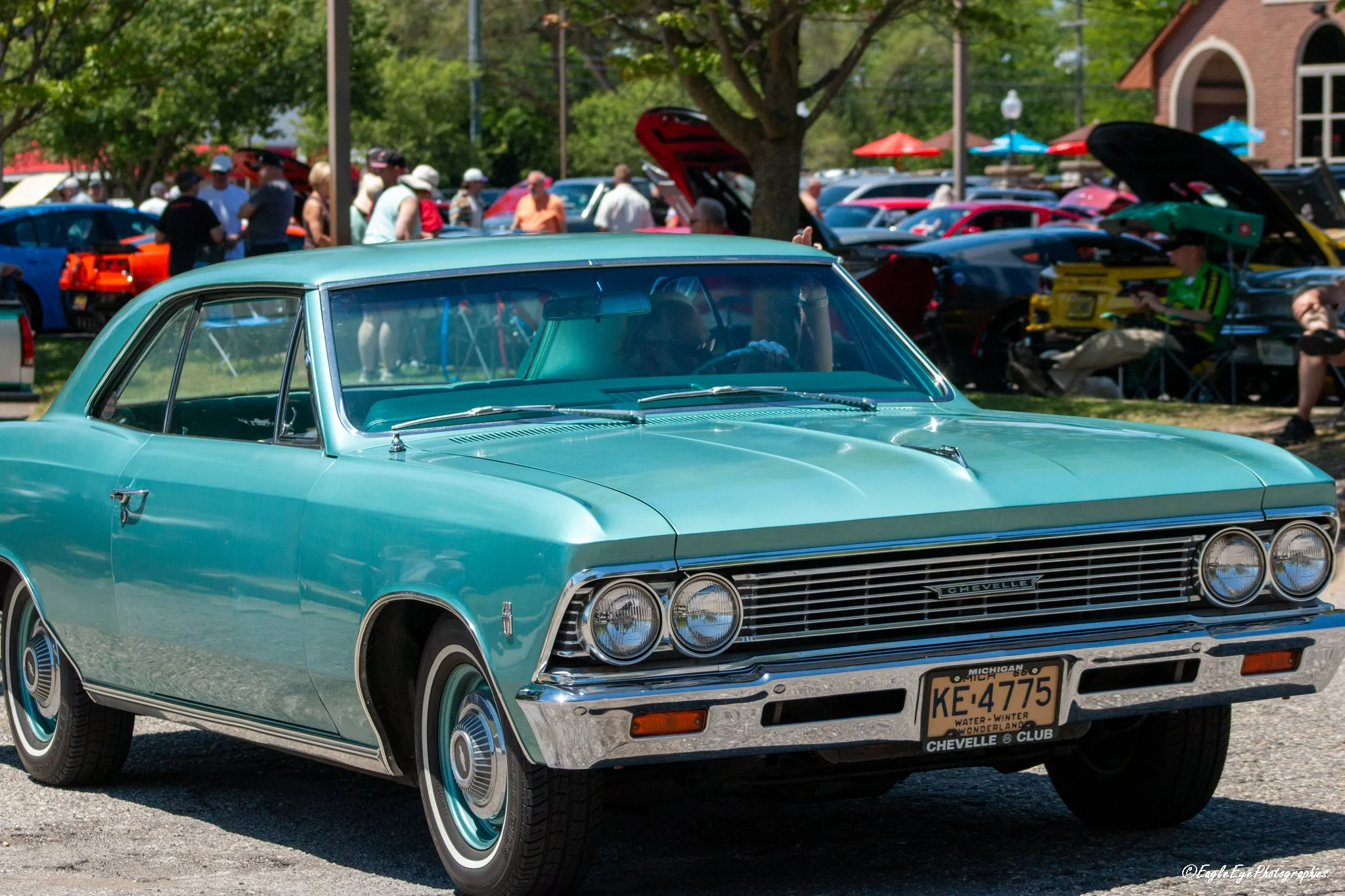 A vintage turquoise Chevrolet car at a classic car show with people walking around and looking at other cars in the background.