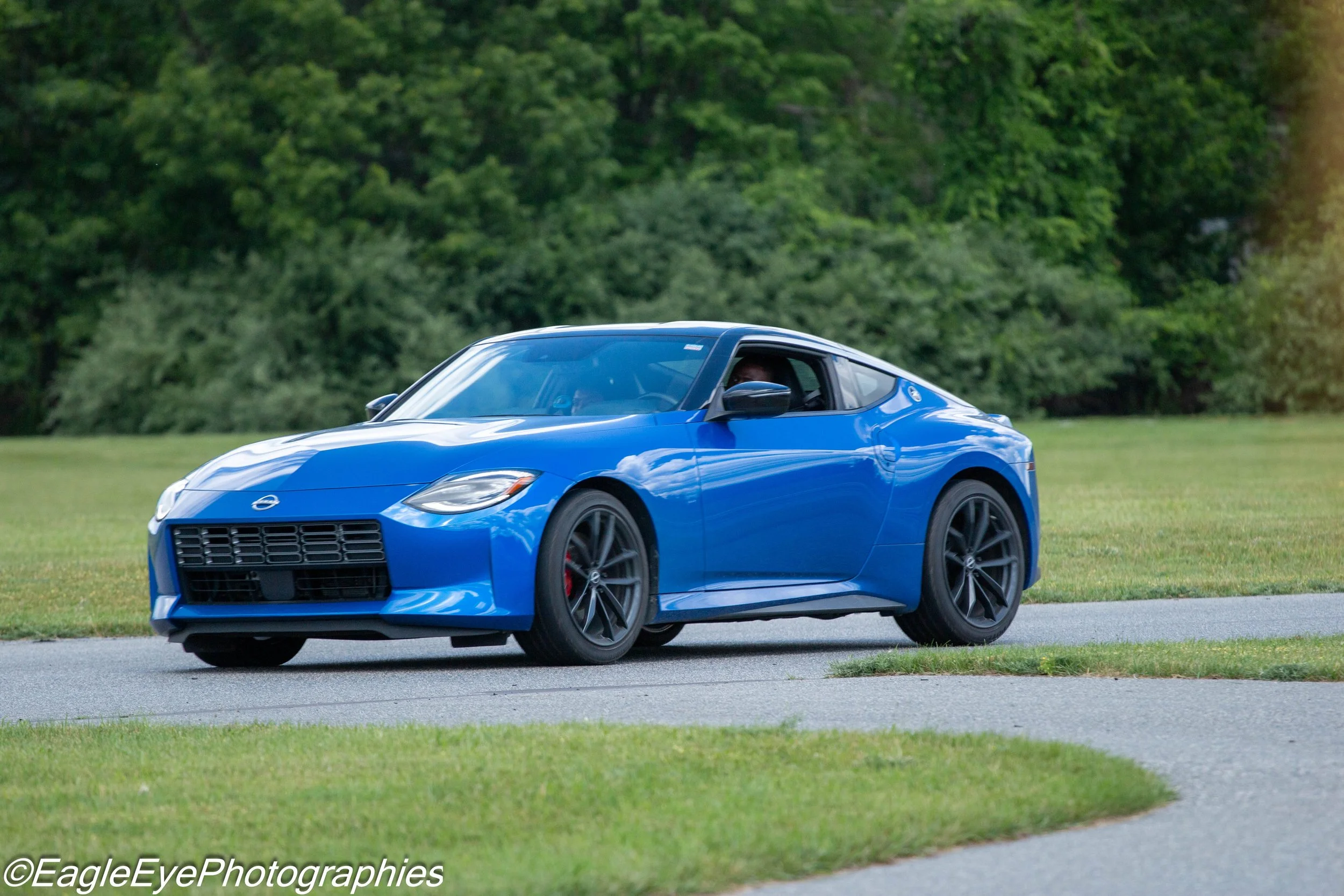 A bright blue sports car driving on a grassy area with trees in the background.