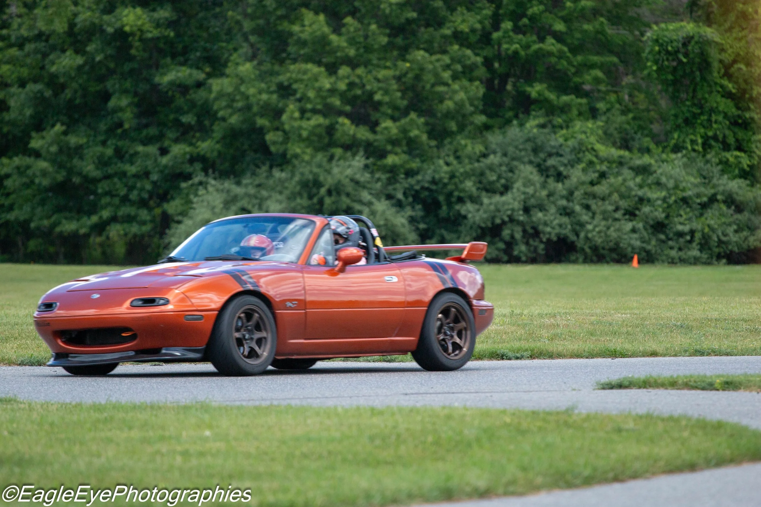 An orange sports car driving on a grassy field with trees in the background.