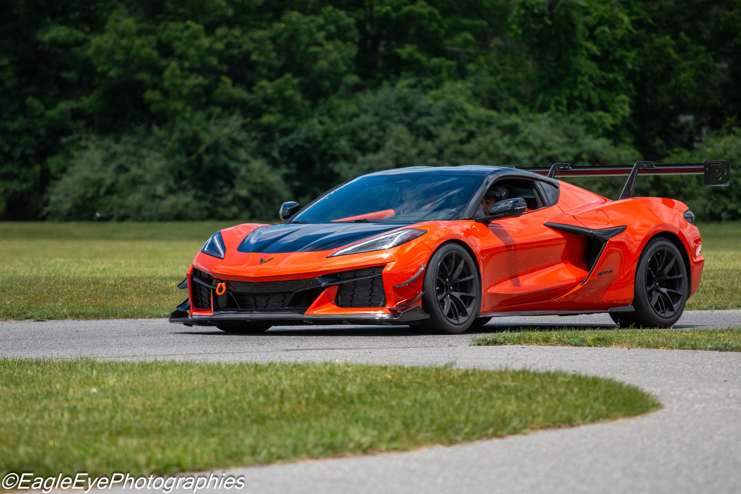 A bright orange sports car driving on a road with a green, forested background.