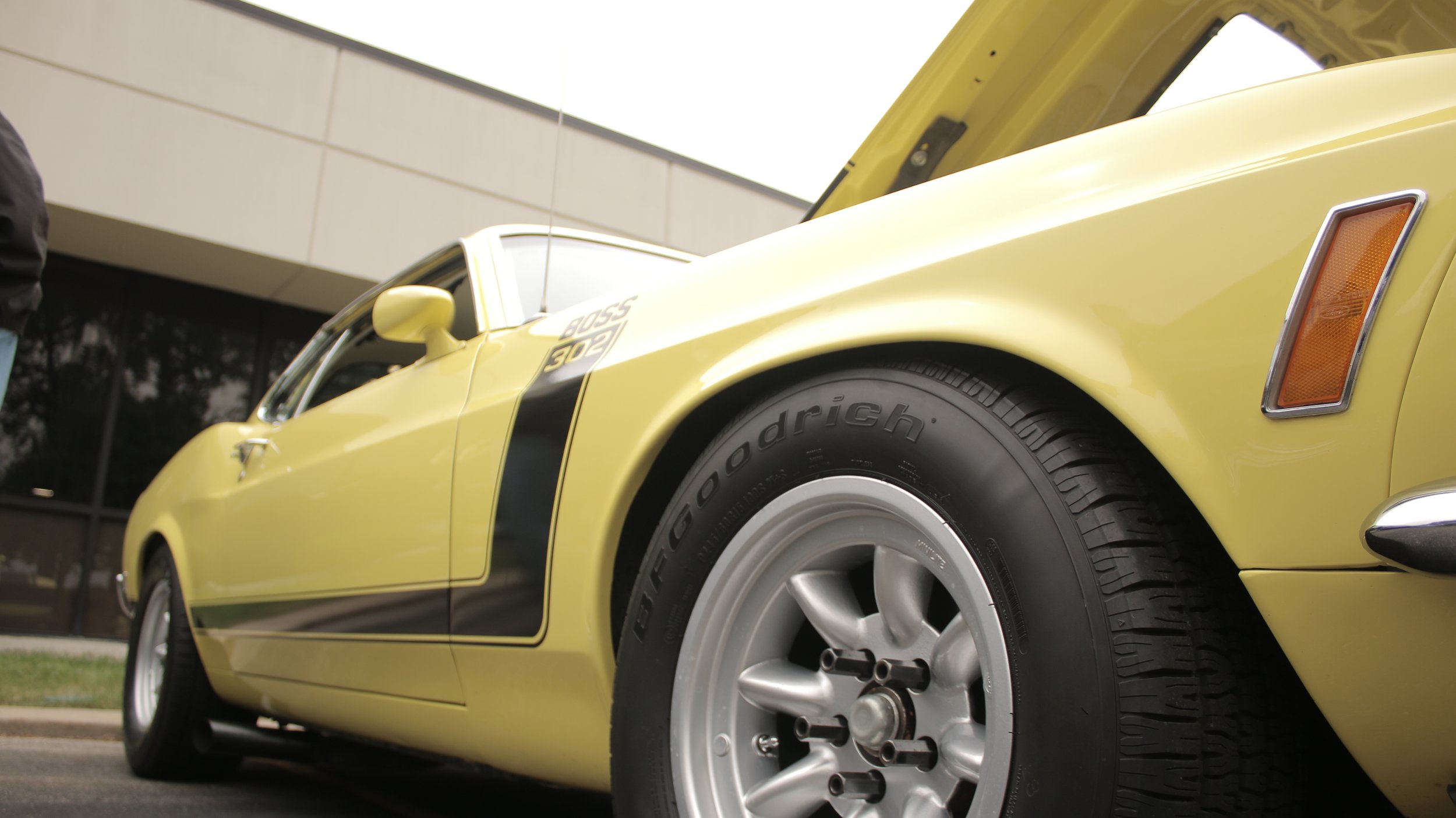 Yellow vintage sports car with open hood, parked outside a modern building.