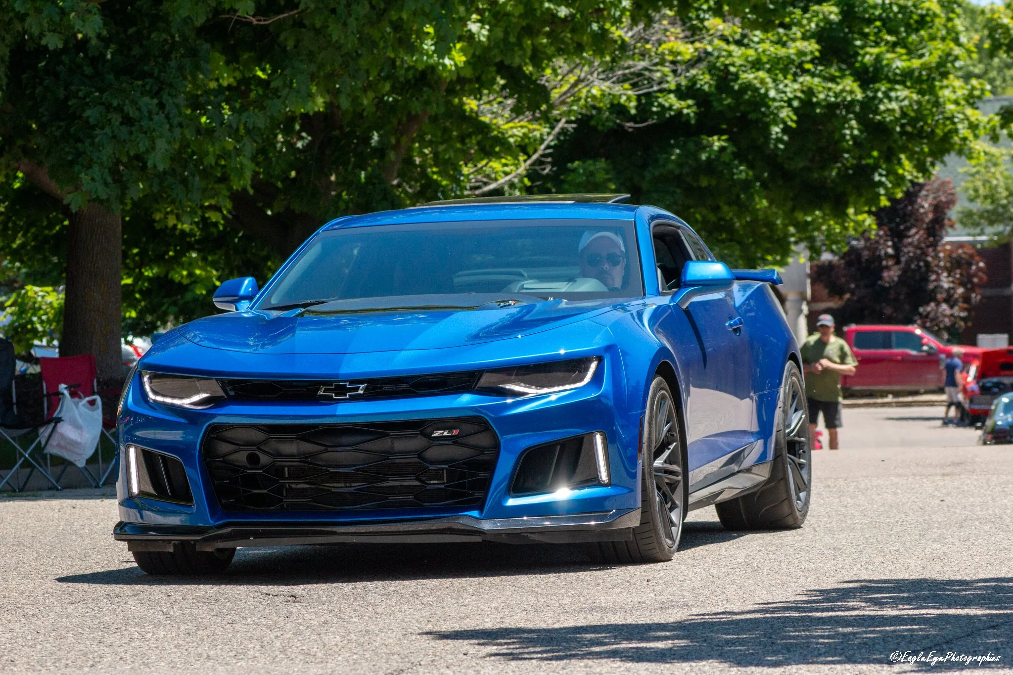 A blue Chevrolet Camaro ZL1 sports car parked outdoors during daytime with trees and people in the background.