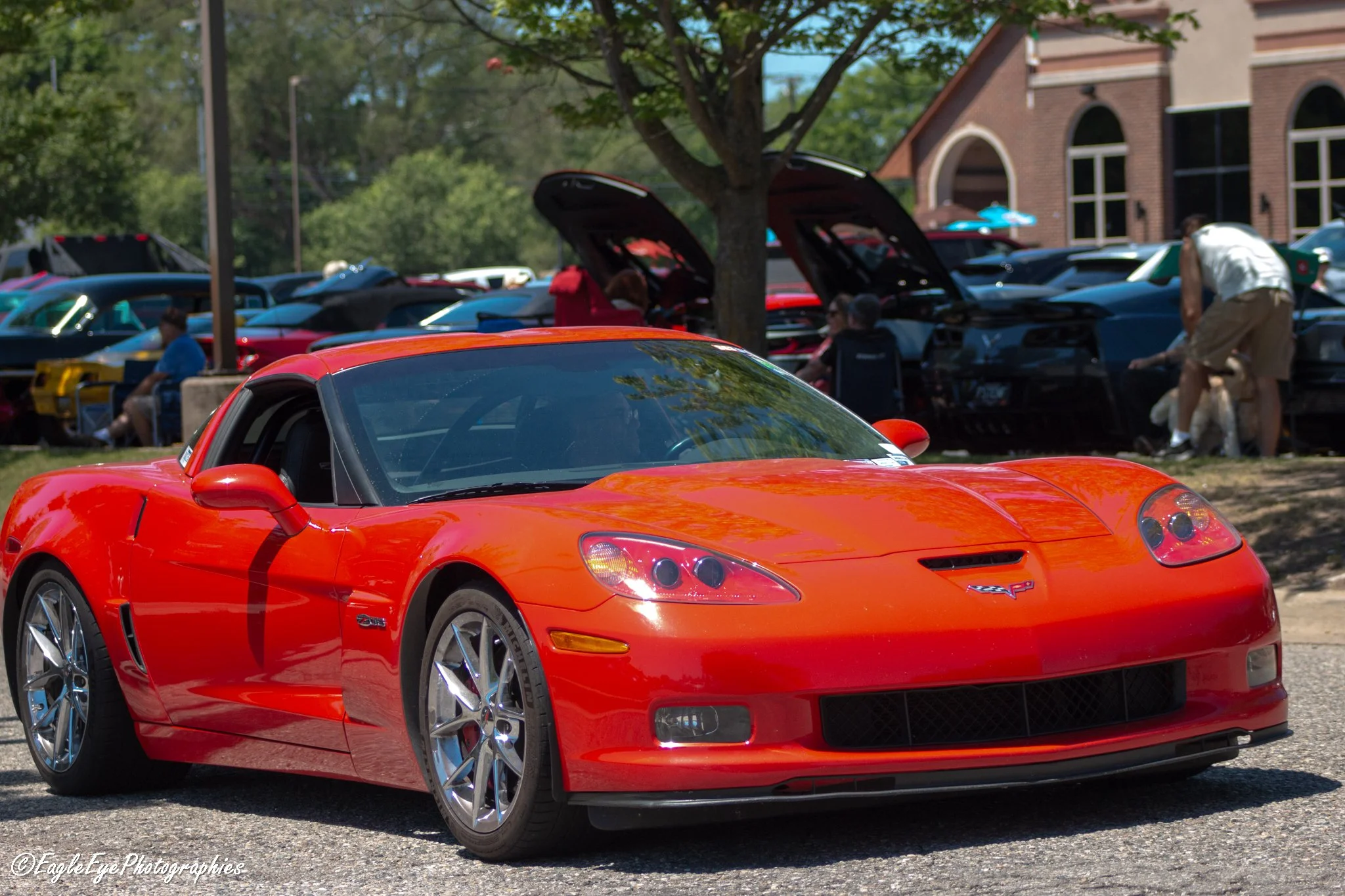 A close-up of a red Chevrolet Corvette sports car parked outdoors, with other cars and people in the background at a car show.