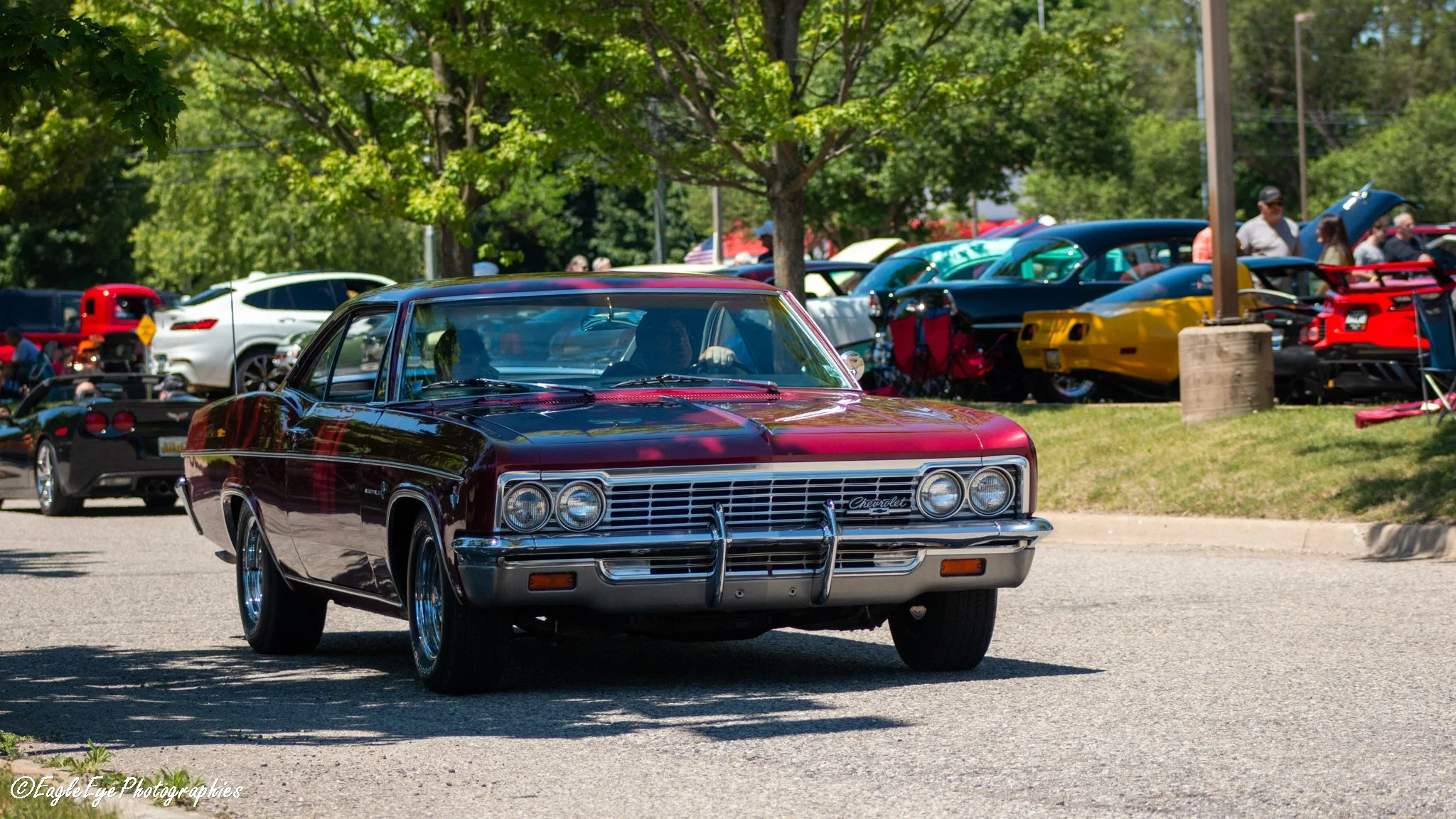A vintage black and red Chevrolet car parked at a car show with other classic cars and people in the background.