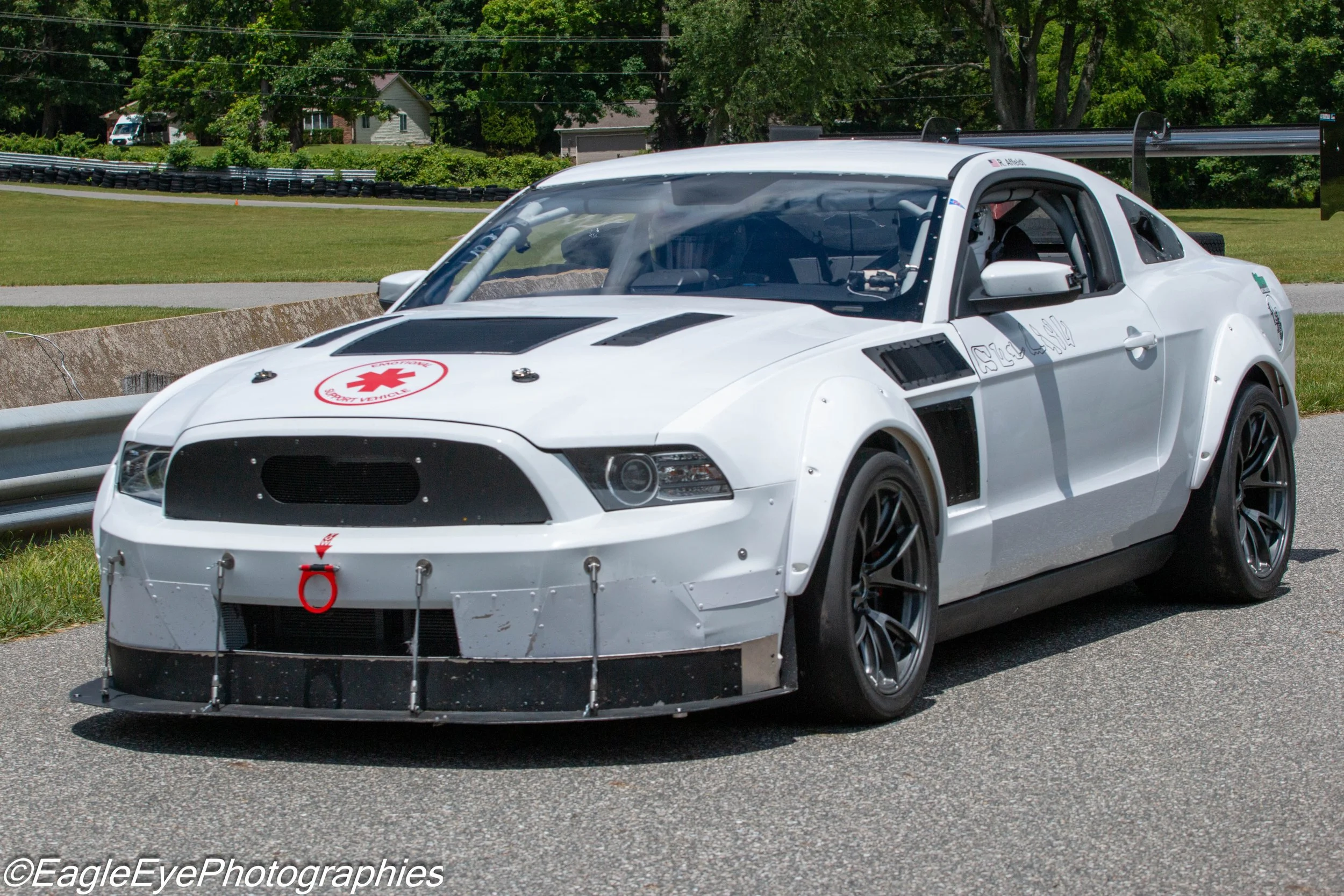 Race car on a track during a racing event, with a white body featuring logo markings and a large rear wing for aerodynamics.