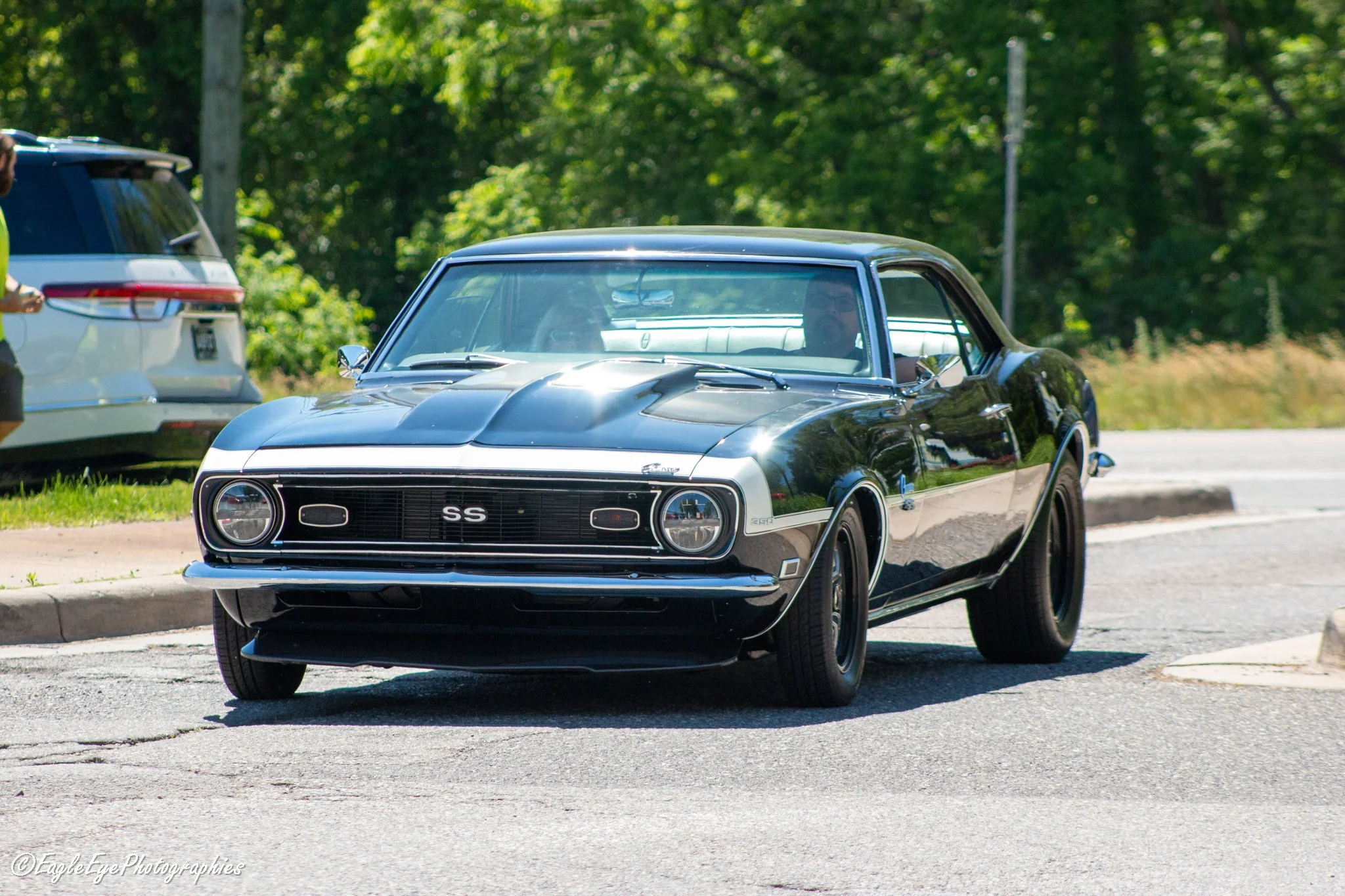 A black Chevrolet Camaro SS muscle car parked on the side of a road with trees in the background.