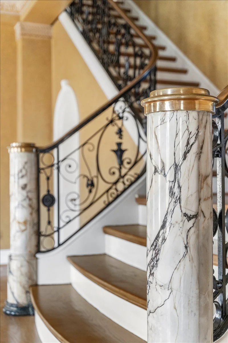 Marble staircase post with gold trim and ornate black metal railing.