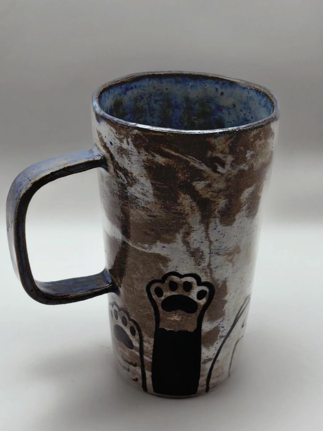 Handmade The Big Furbowski Ceramic mug with a paw print design, brown and blue glaze inside and outside, on a plain surface.