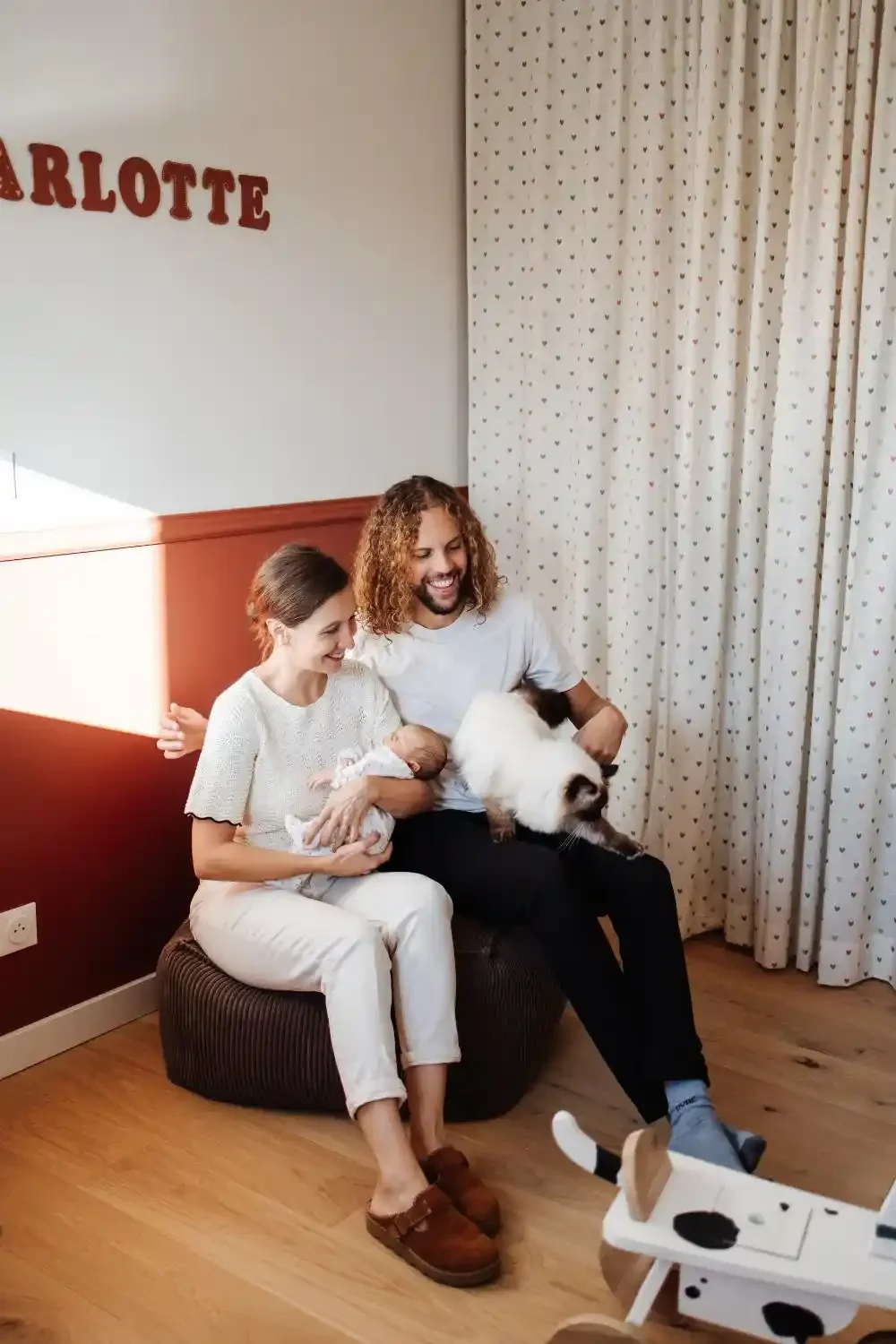 Parents assis sur un pouf avec leur nouveau-né, le chat de la famille à côté, séance photo naissance à domicile à Villeneuve-d’Ascq