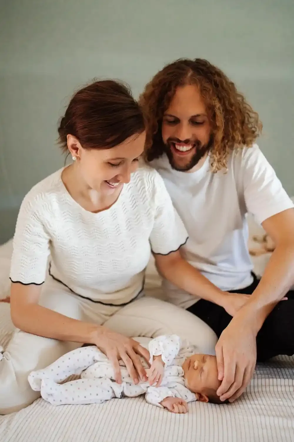 Maman et papa rient en caressant leur nouveau-né allongé sur le lit, souvenirs de naissance à Villeneuve-d’Ascq